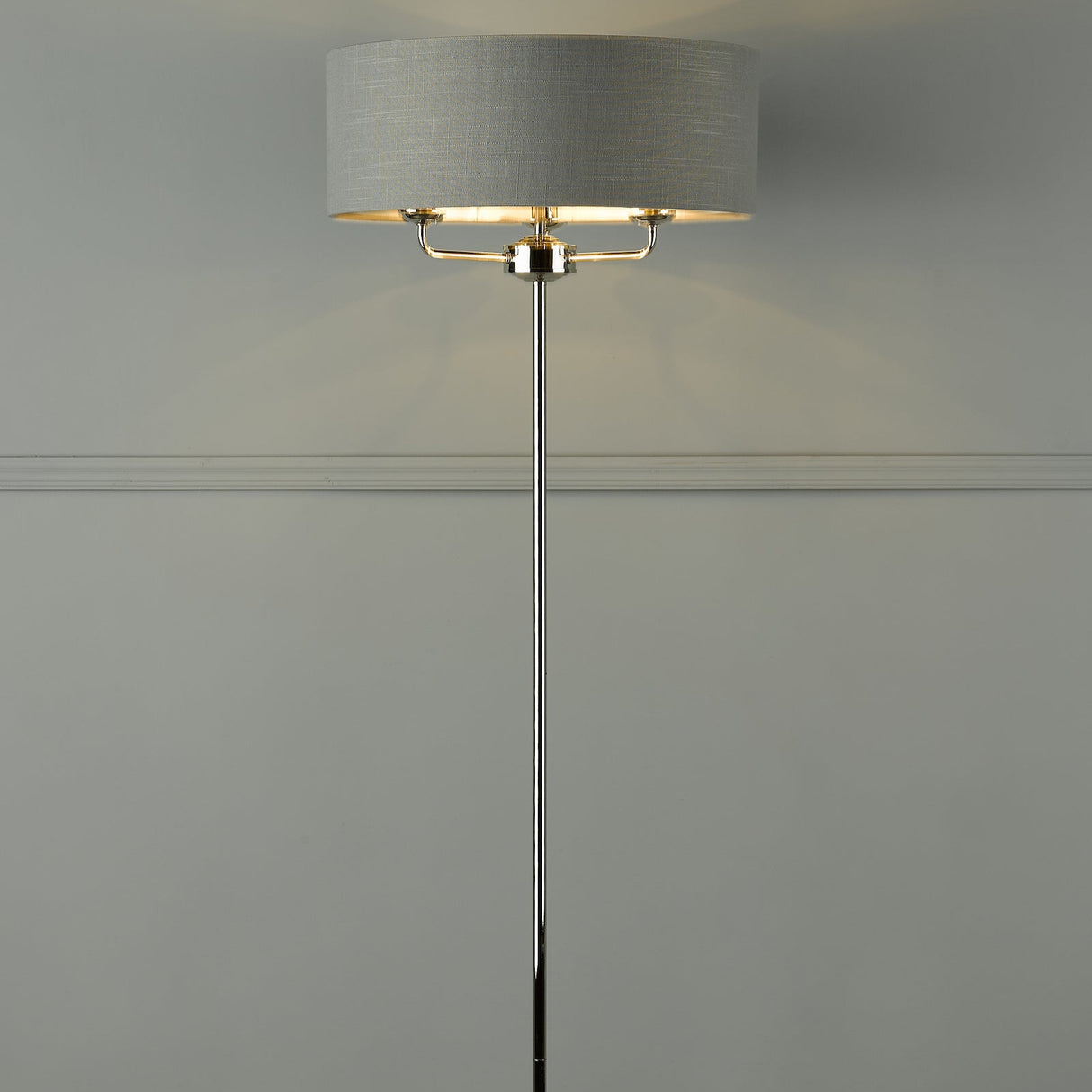 Modern floor lamp with chrome stand and textured gray drum shade against light gray wall