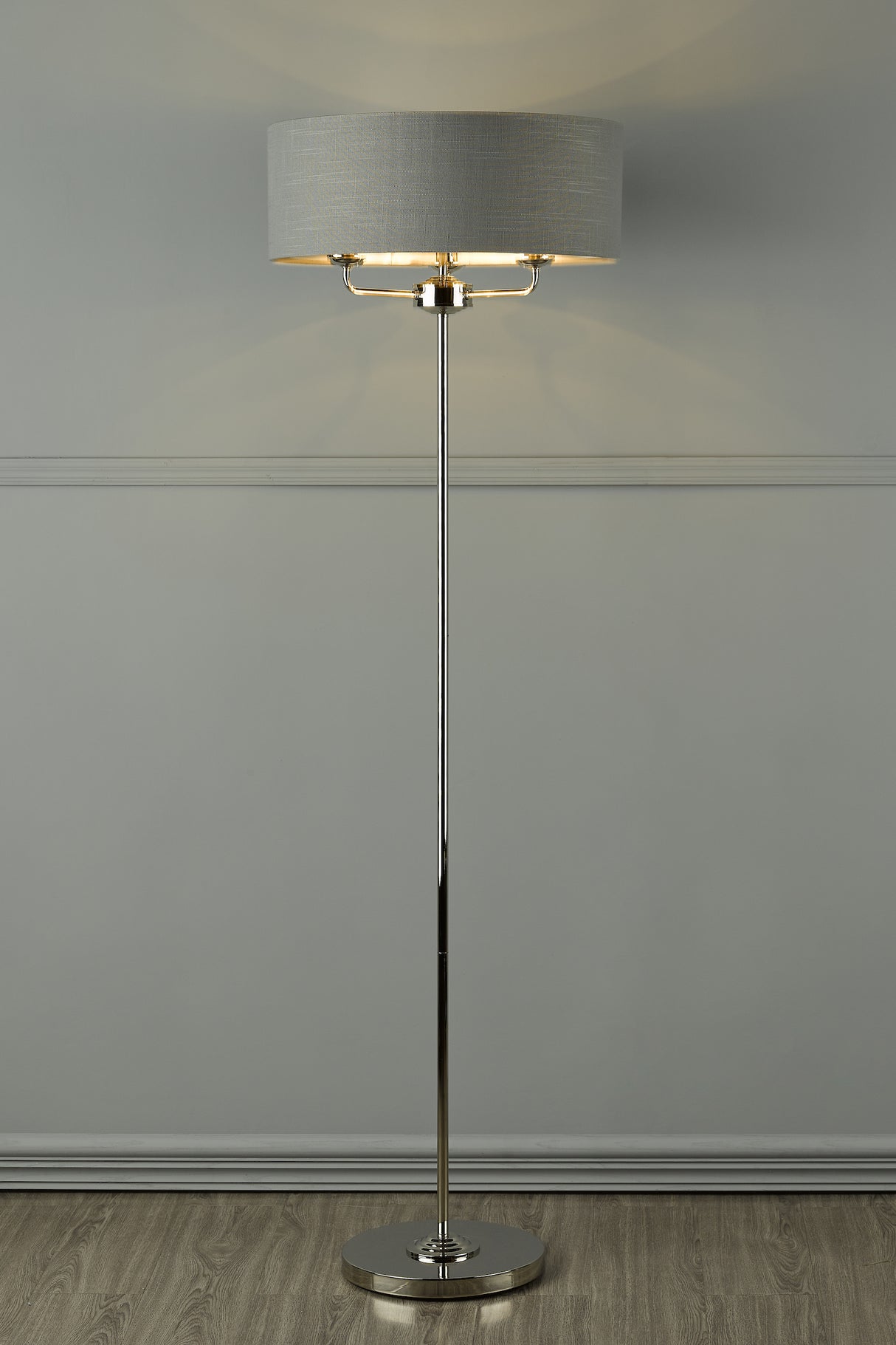 Modern floor lamp with chrome stand and gray fabric drum shade on wood floor
