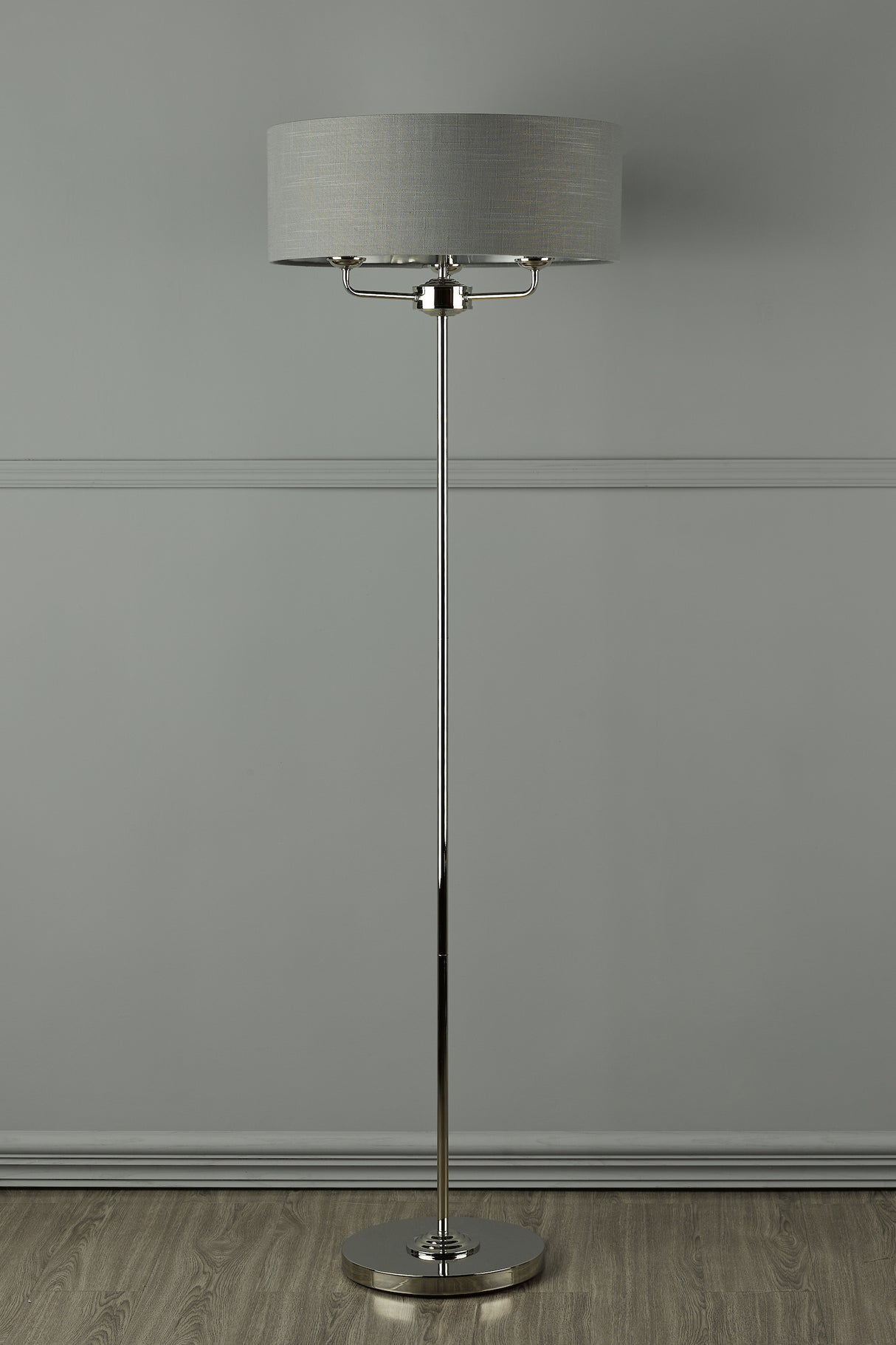 Modern chrome floor lamp with gray fabric drum shade on wood floor against gray wall
