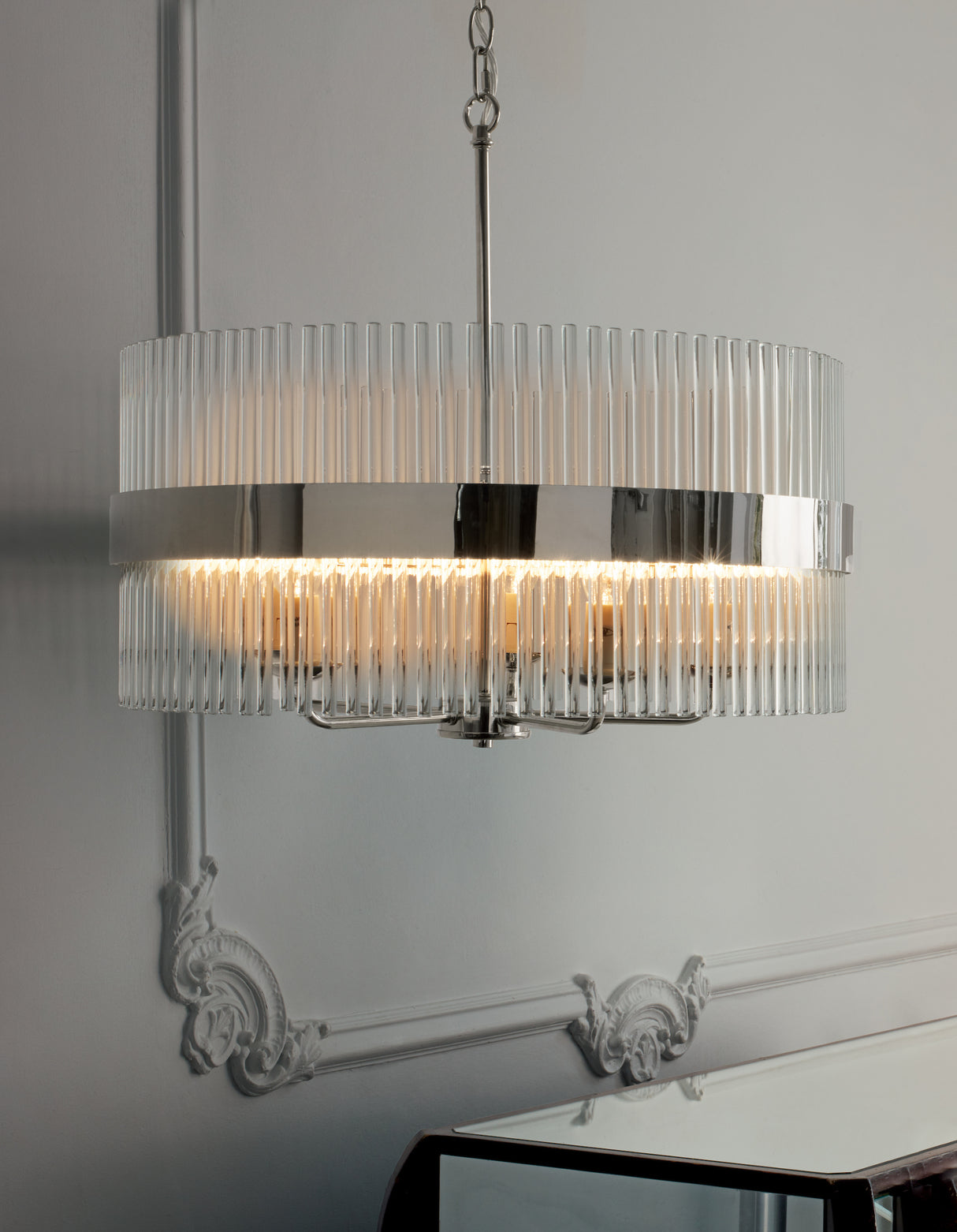 Modern chandelier with vertical glass rods and chrome band hanging in elegant interior