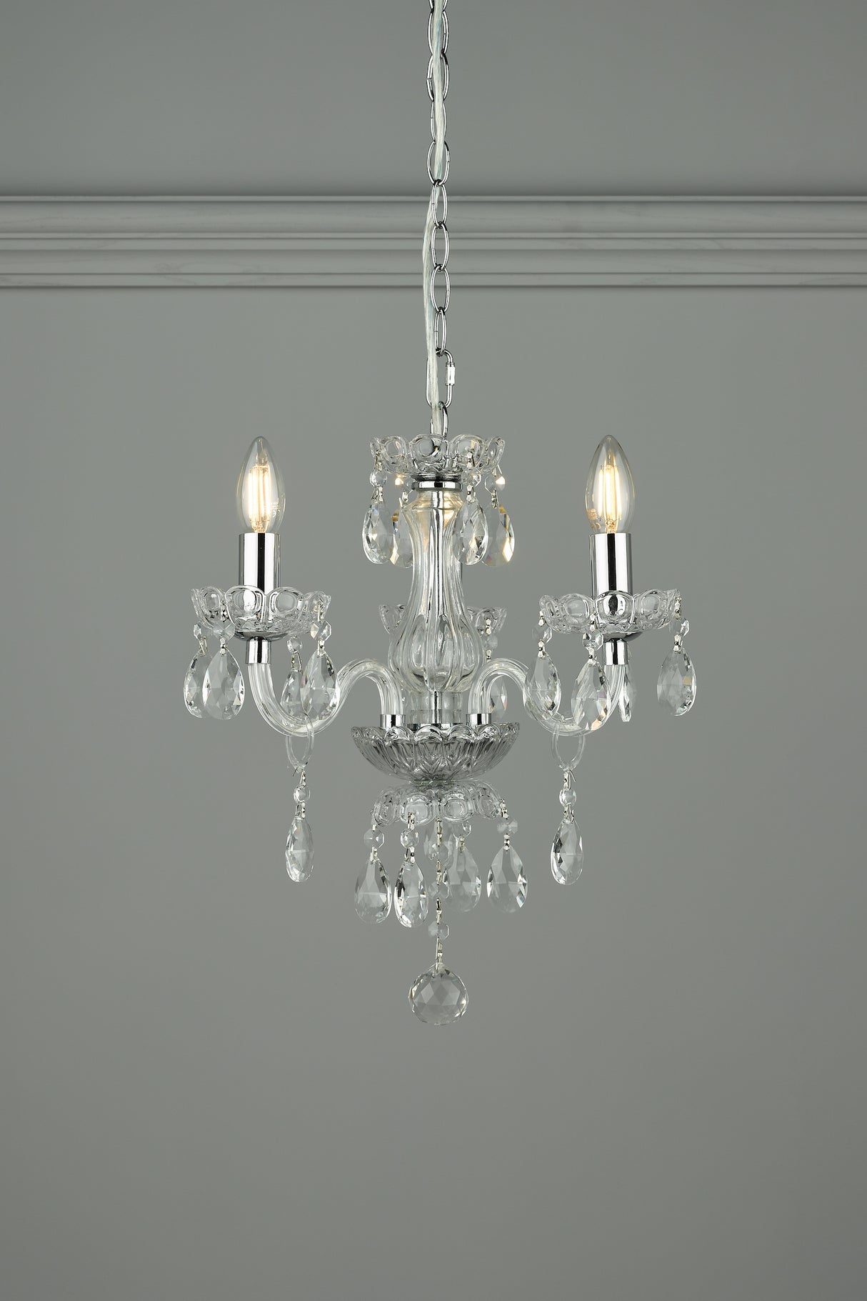Elegant two-light crystal chandelier with hanging glass prisms and silver chain against gray wall
