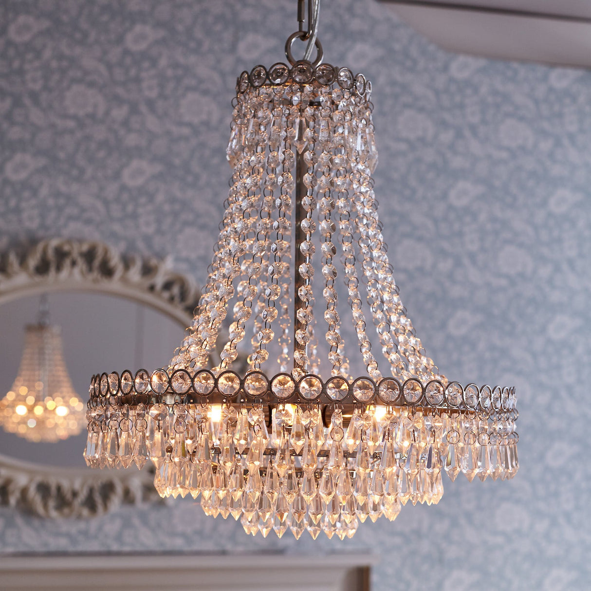 Elegant crystal chandelier hanging in a room with patterned wallpaper and a decorative mirror