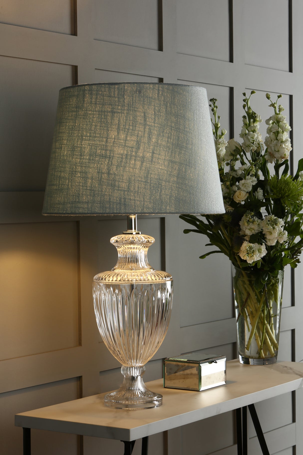 Elegant glass table lamp with textured blue shade on white console table with flowers