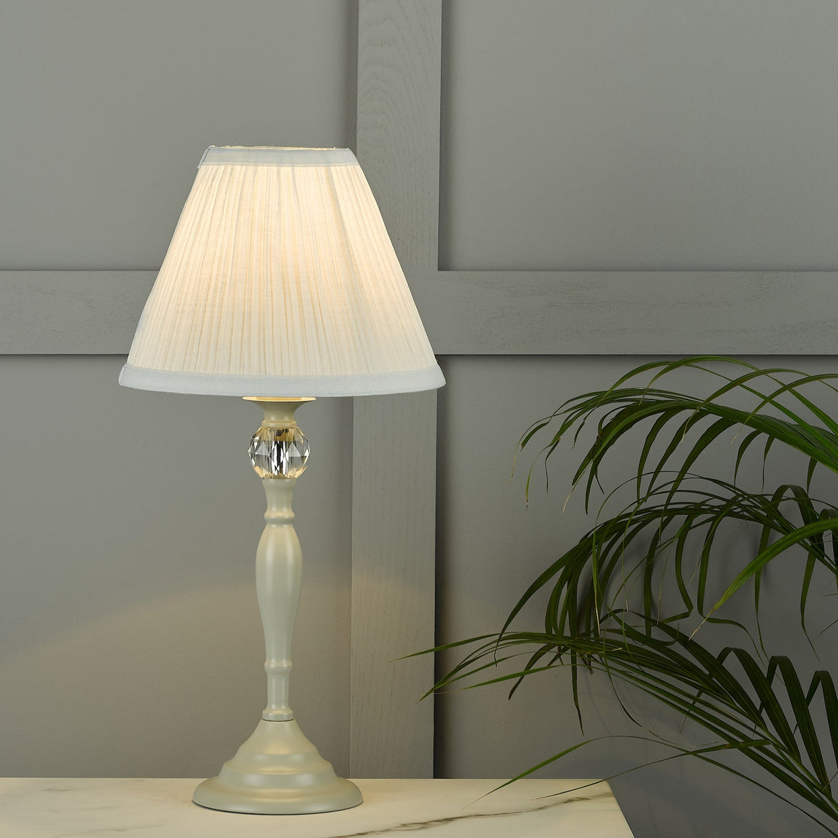 Elegant white table lamp with pleated shade and crystal accent on marble surface by grey wall