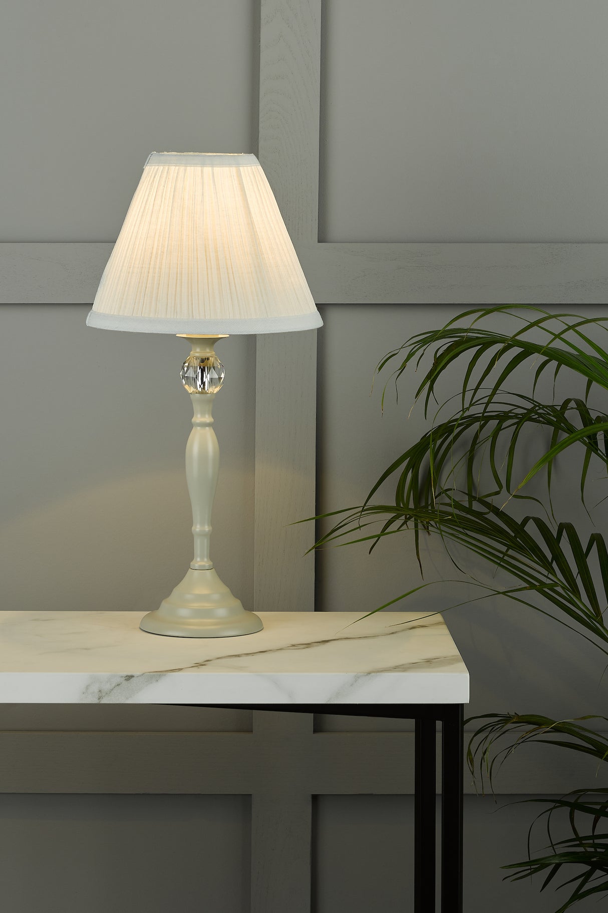Elegant white table lamp with pleated shade on marble top table beside green plant