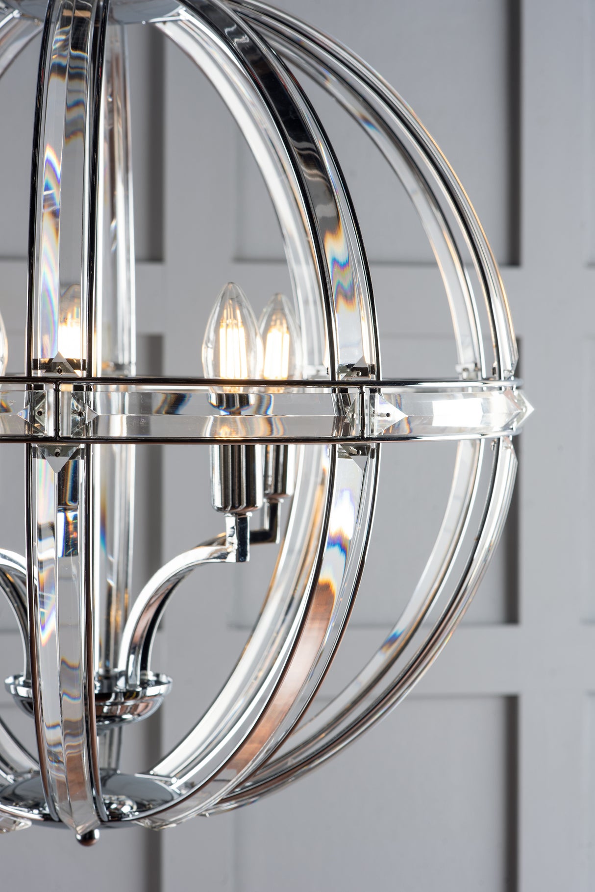 Chrome spherical chandelier with candle-style bulbs against gray paneled wall