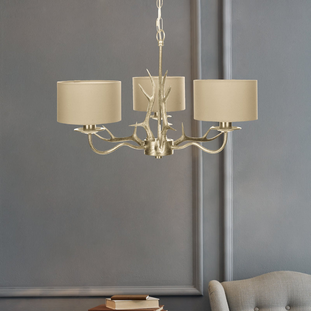Gold antler chandelier with three beige lampshades hanging in modern gray living room
