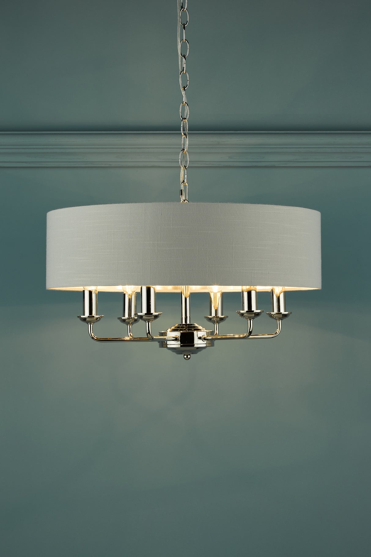 Modern chandelier with white fabric drum shade and polished metal arms on chain in room