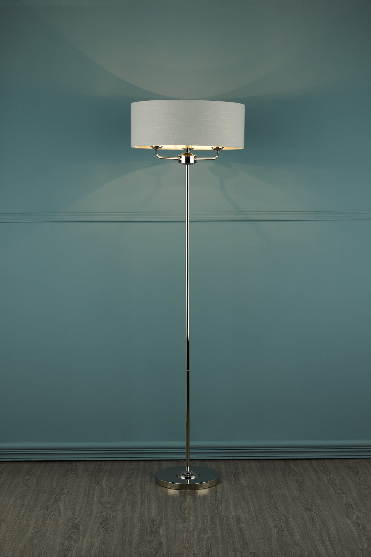 Modern floor lamp with white fabric drum shade and chrome base on wooden floor