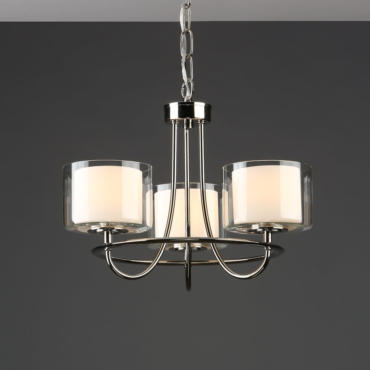 Modern three-light chandelier with chrome finish and cylindrical frosted glass shades on dark background