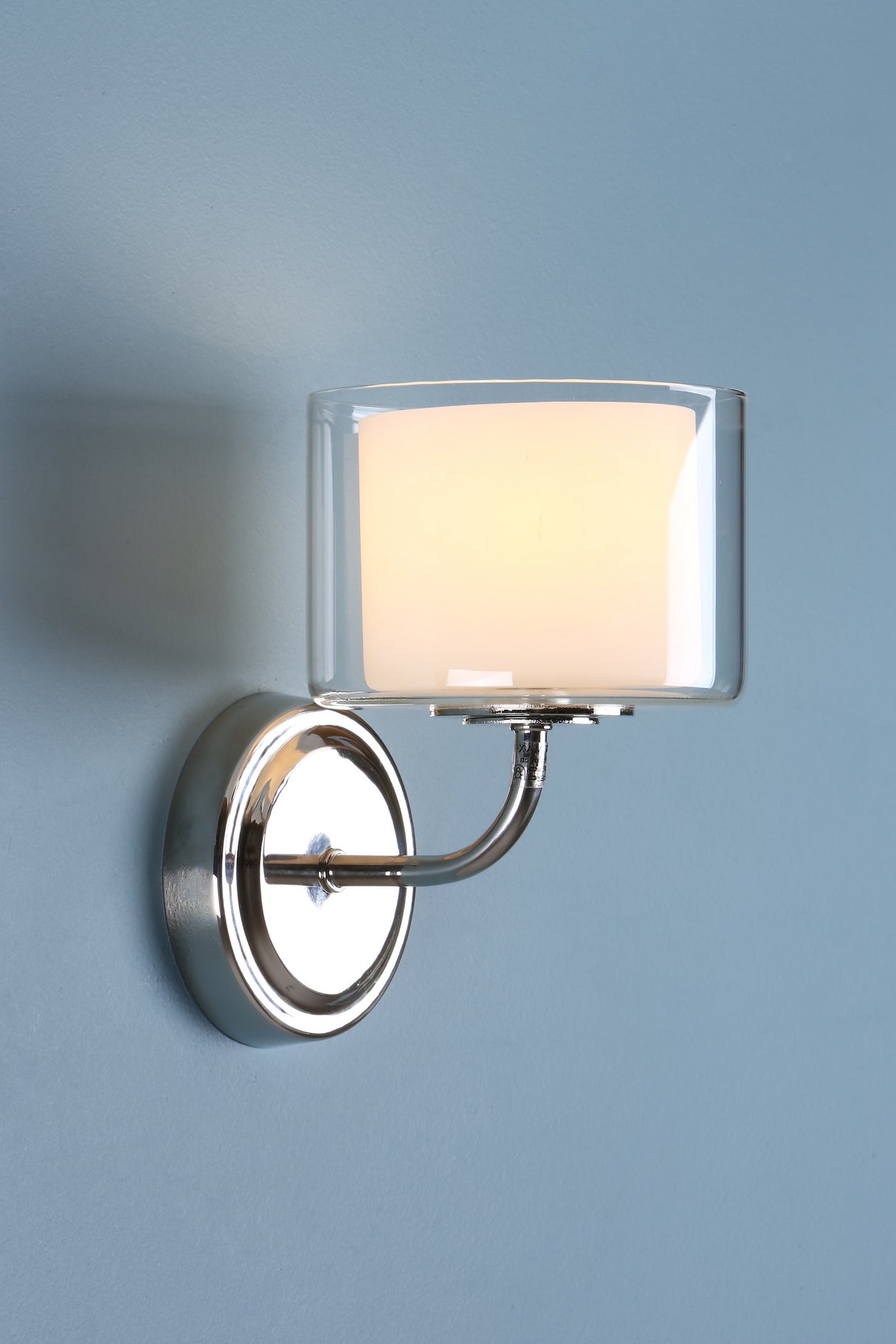 Modern wall sconce with chrome base and frosted glass shade on blue wall