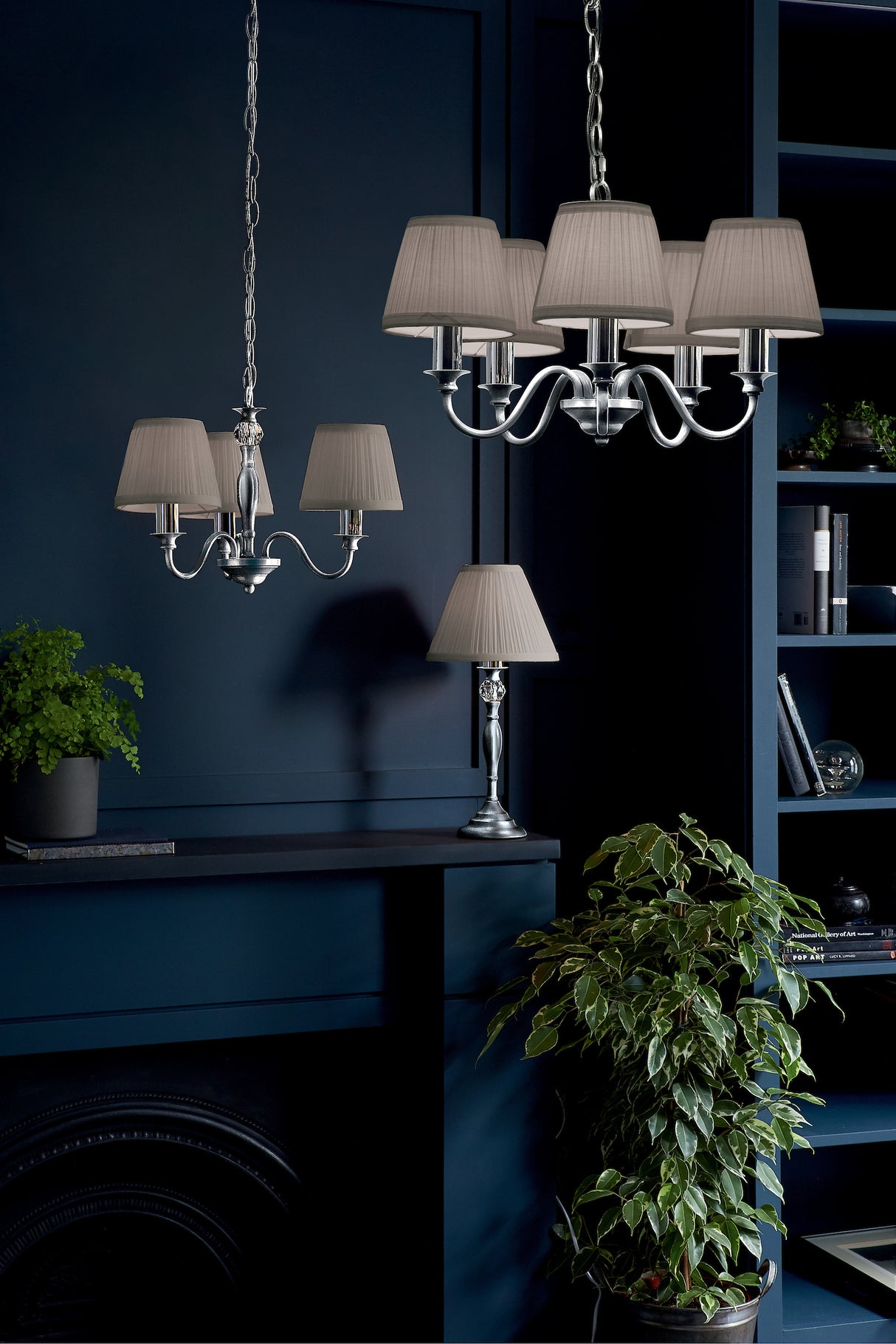 Modern navy blue interior with silver chandeliers, table lamp, bookshelf, and green plants