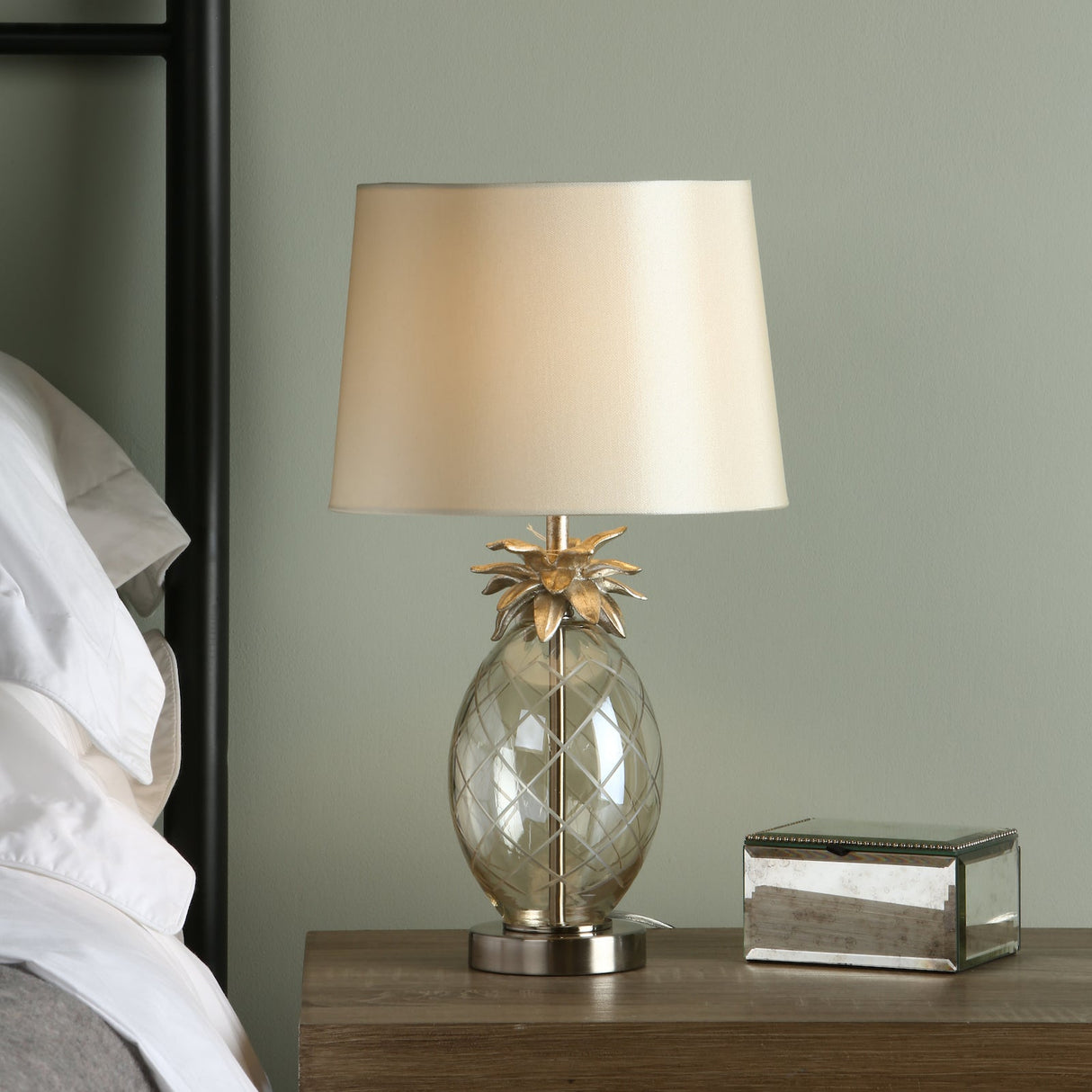 Modern pineapple-shaped table lamp with beige shade on wooden nightstand next to white bed linens
