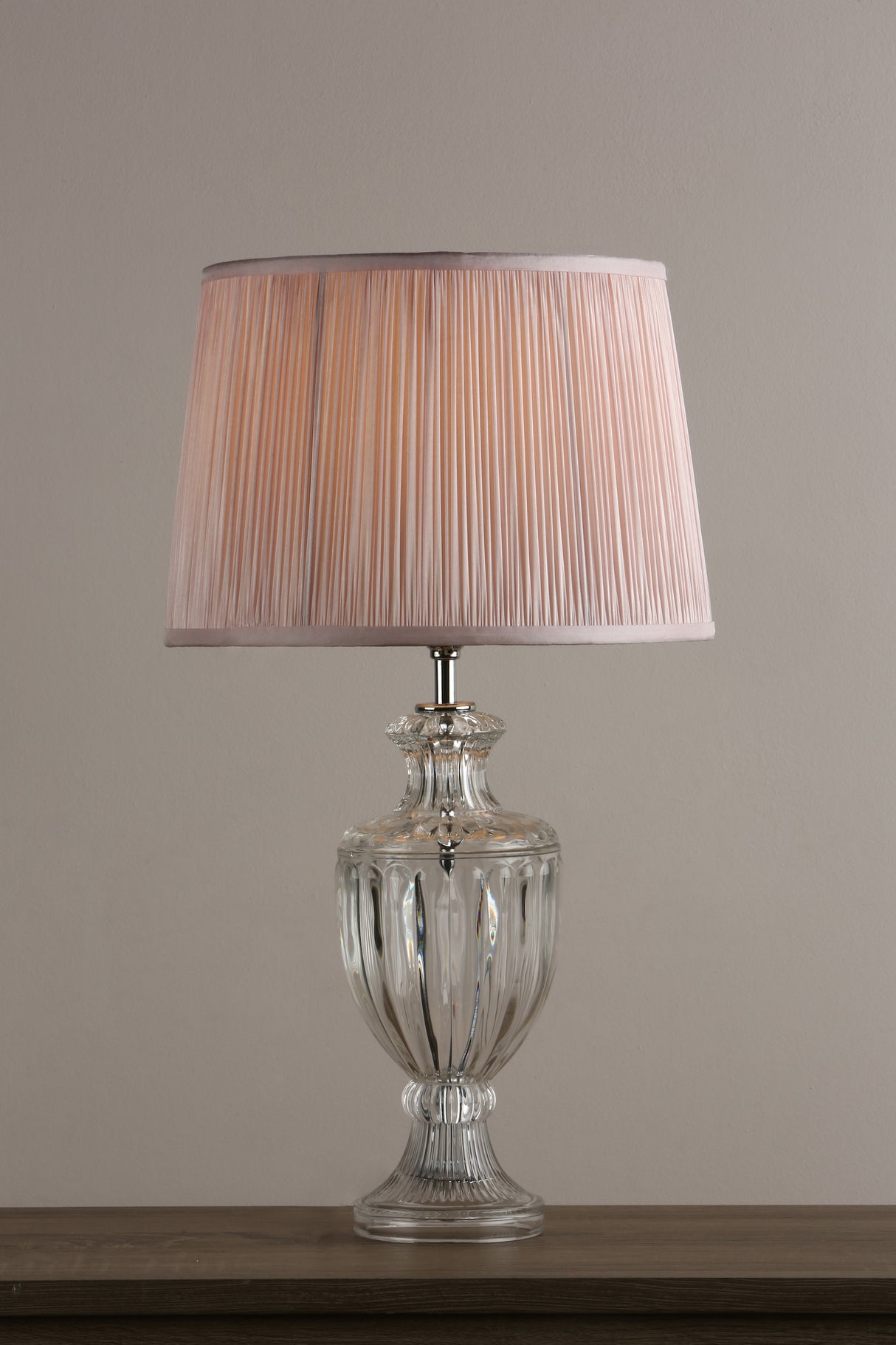 Elegant table lamp with a pleated beige fabric shade and a clear glass base on wooden surface
