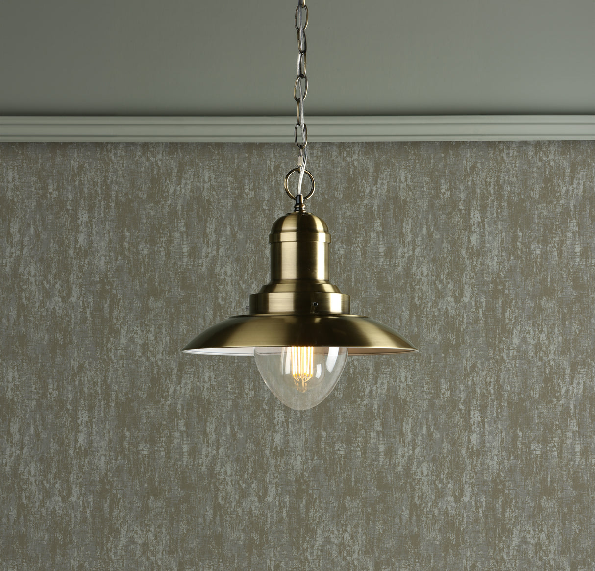 Brass pendant industrial style light fixture with clear bulb hanging from silver chain against textured gray wall