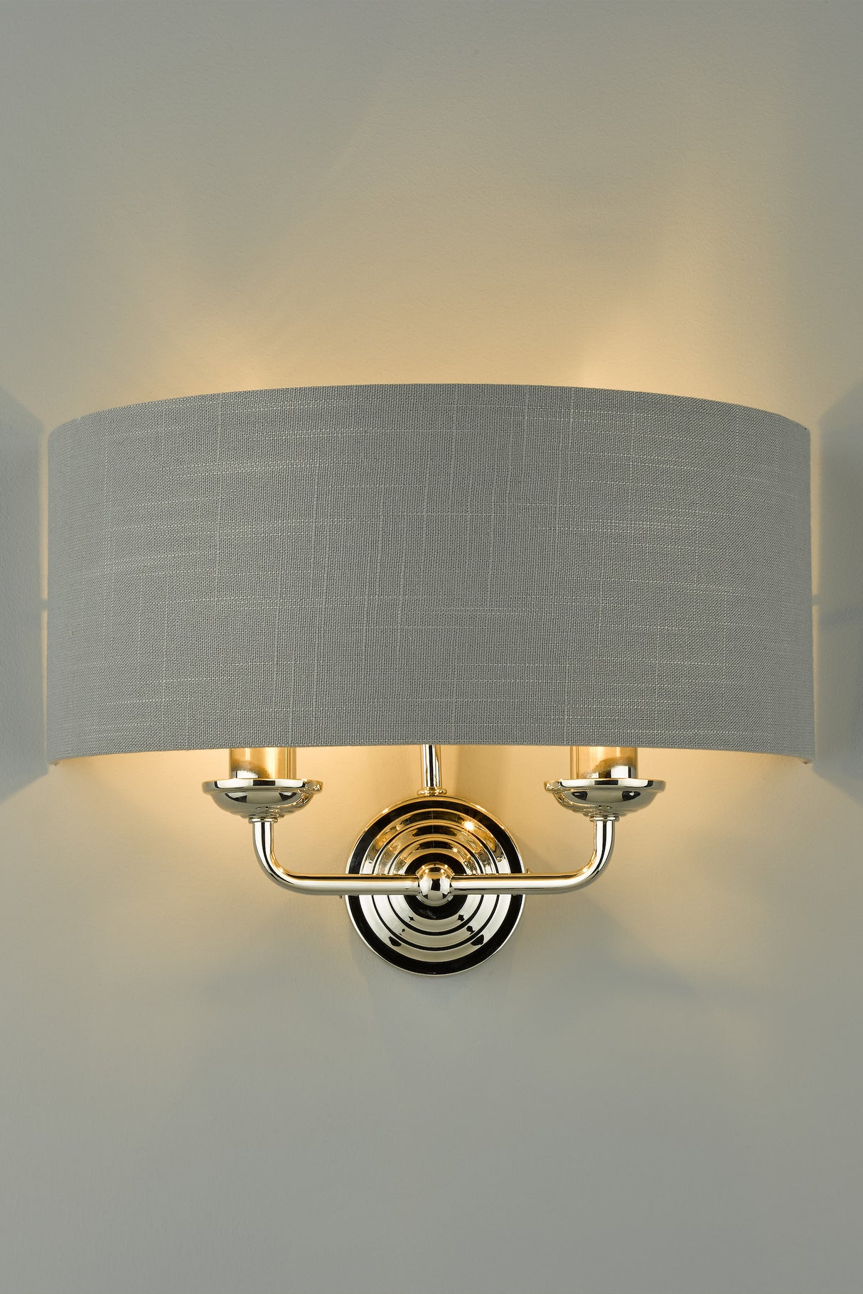 Modern wall sconce with gray fabric shade and polished chrome base lighting a neutral wall