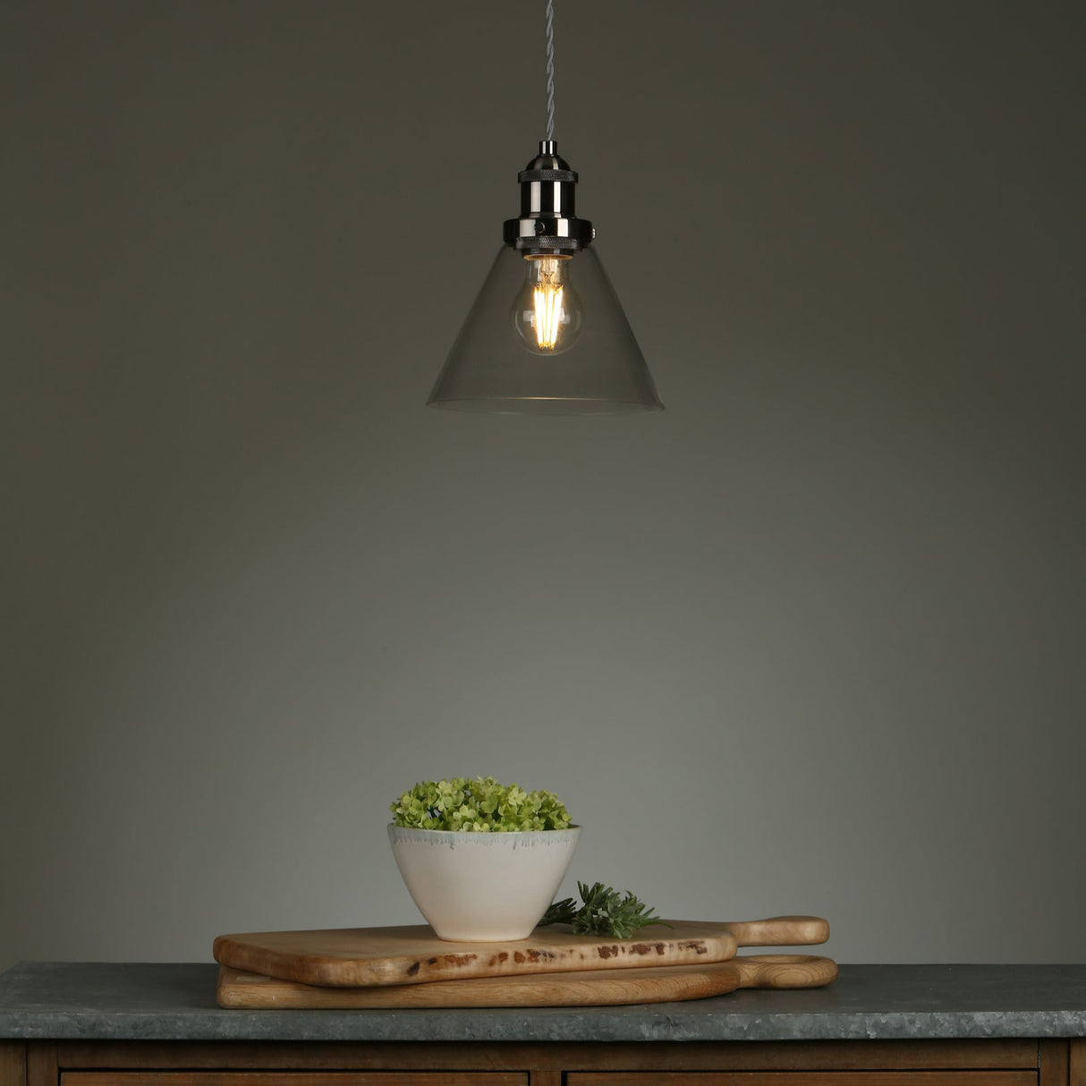 Modern pendant light over wooden cutting boards with a white bowl of green flowers on a kitchen countertop