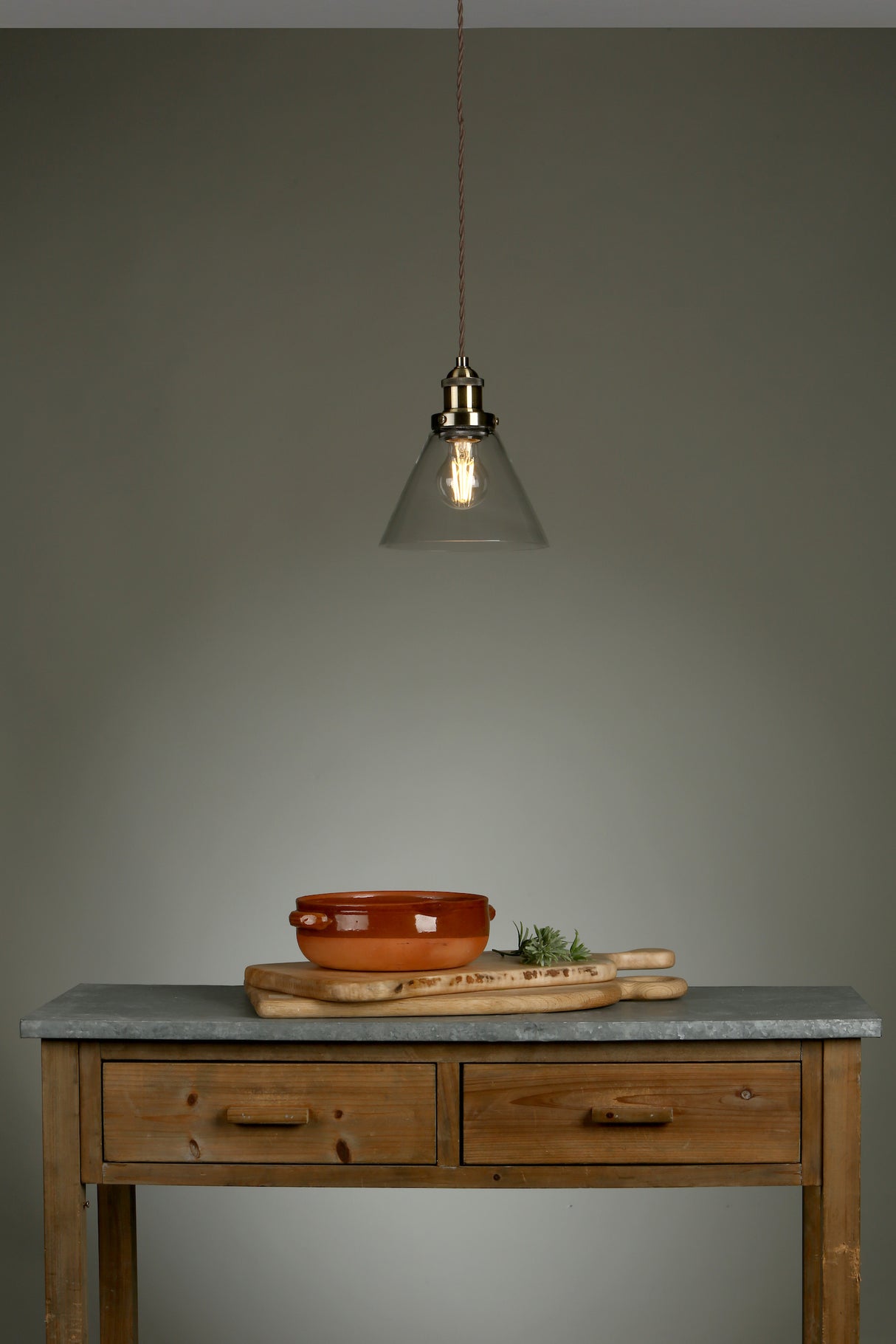 Rustic wooden table with gray countertop, terracotta pot, wooden cutting boards, and hanging pendant light