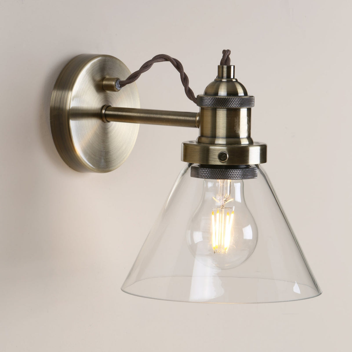 Industrial wall sconce with brass finish and clear glass shade featuring an exposed filament bulb