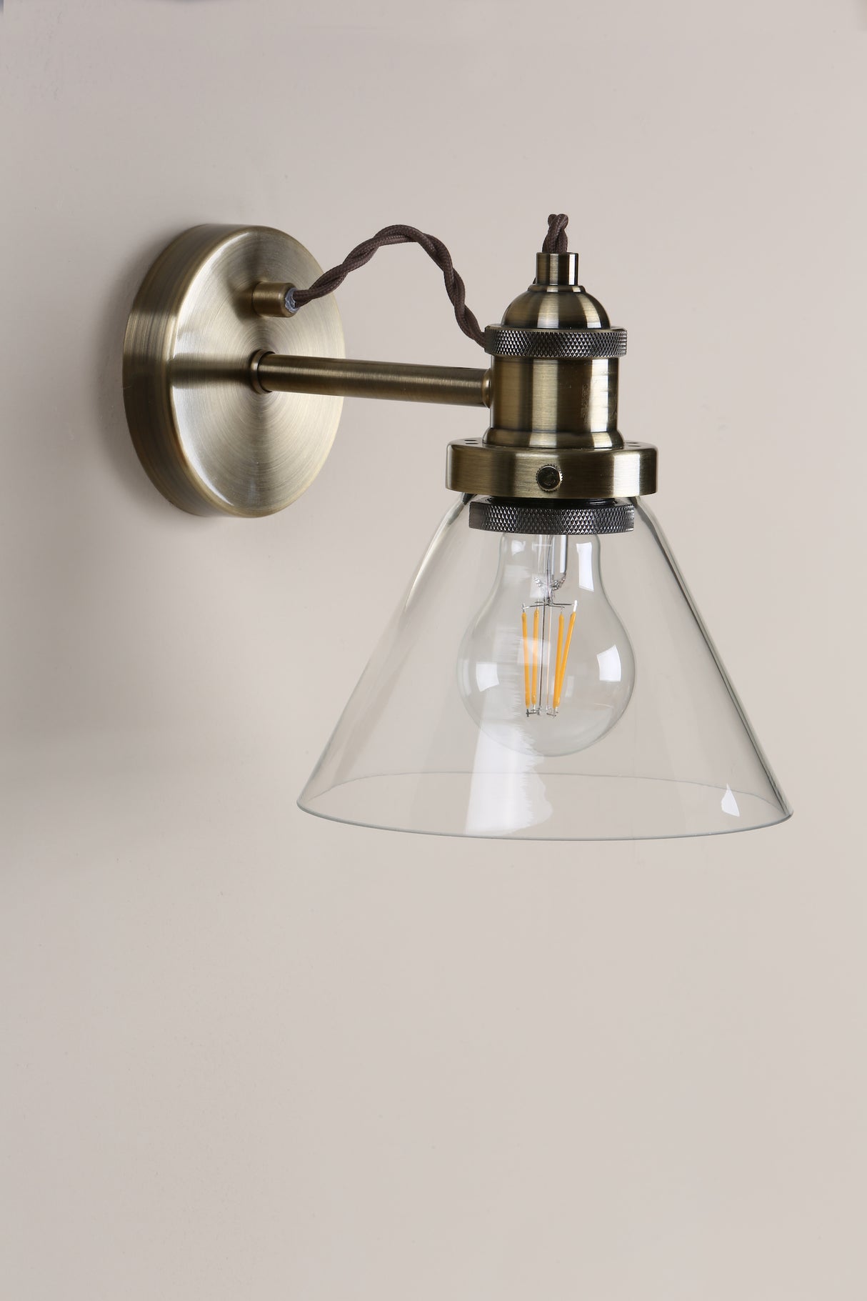 Vintage brass wall sconce with clear glass shade and filament bulb on beige wall
