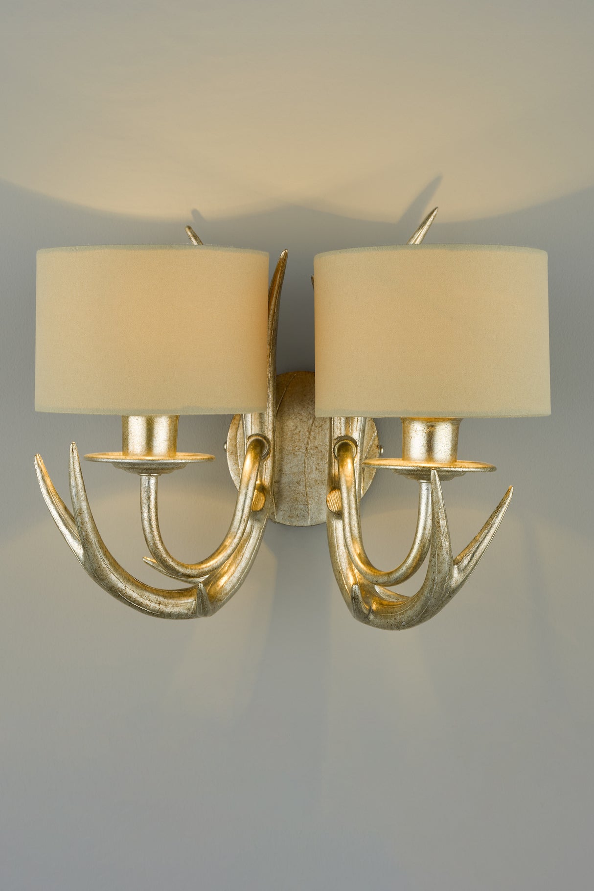 Modern wall sconce with dual beige fabric shades and gold antler-shaped metal arms