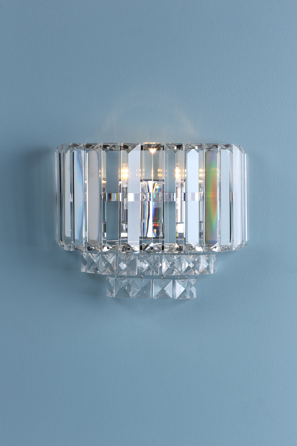 Modern crystal wall sconce with rectangular prisms and hanging crystal accents against blue wall