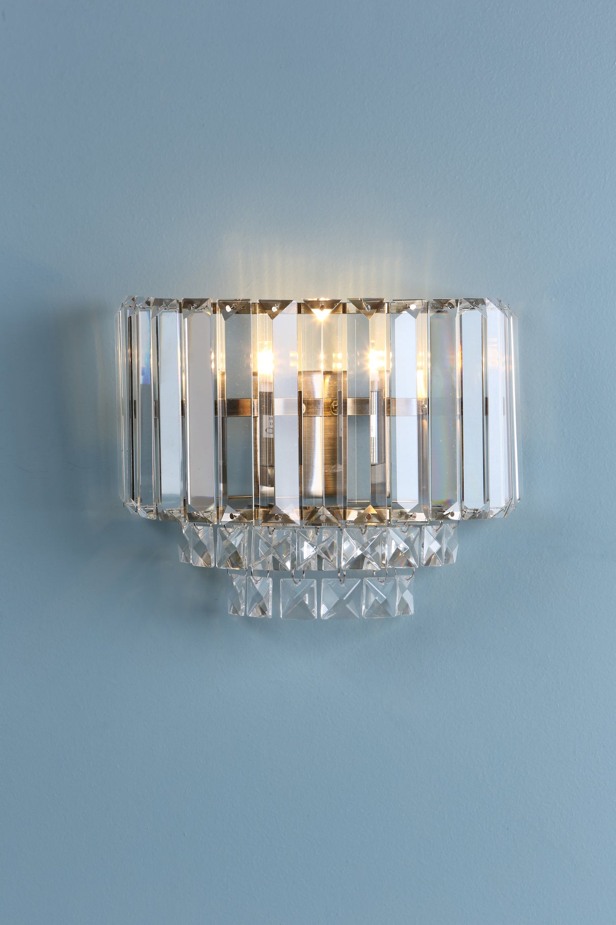 Crystal wall sconce light fixture with brass accents on light blue wall