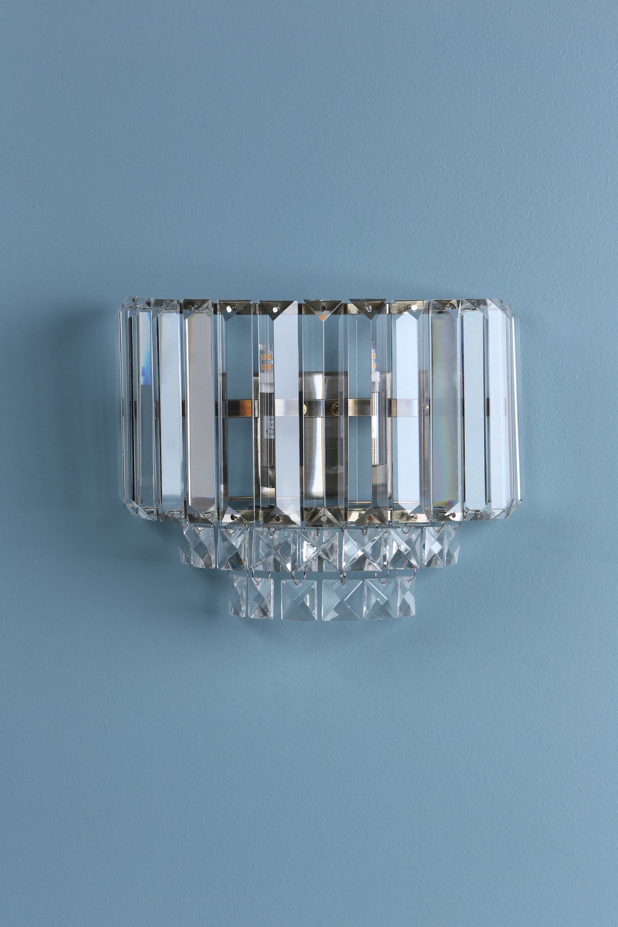 Modern crystal wall sconce light fixture mounted on blue wall with geometric glass design