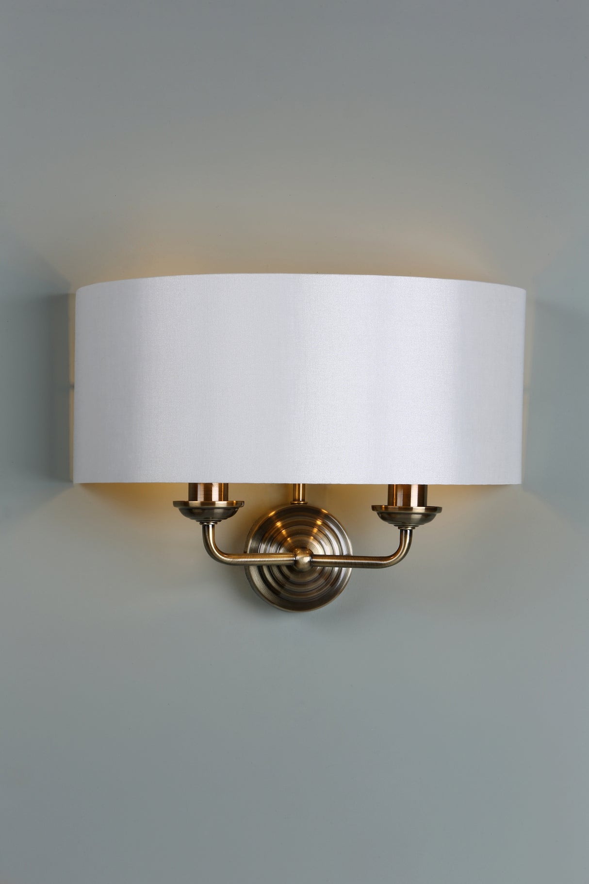 Brass wall sconce light fixture with white fabric drum shade on gray wall