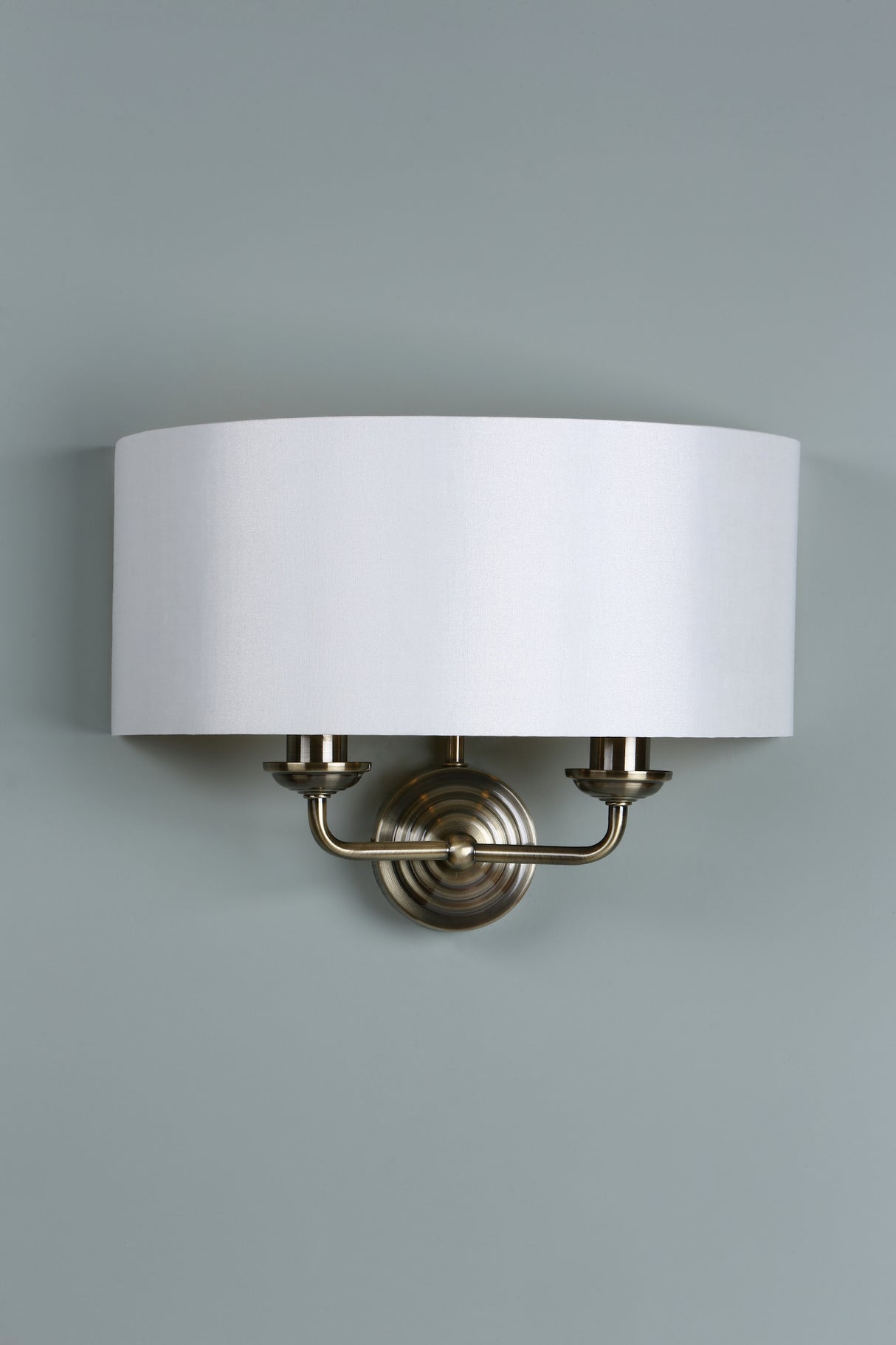 Modern wall sconce with white fabric shade and brushed brass finish against gray wall