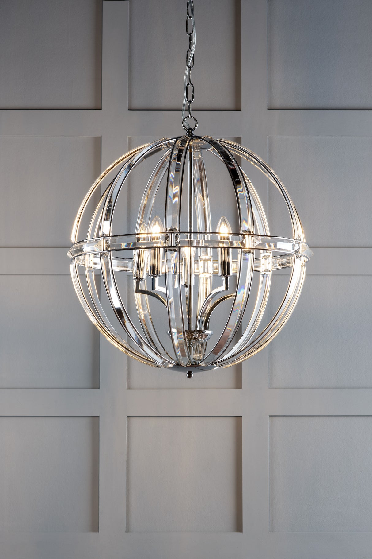 Modern chrome orb chandelier with exposed bulbs hanging against a gray paneled wall