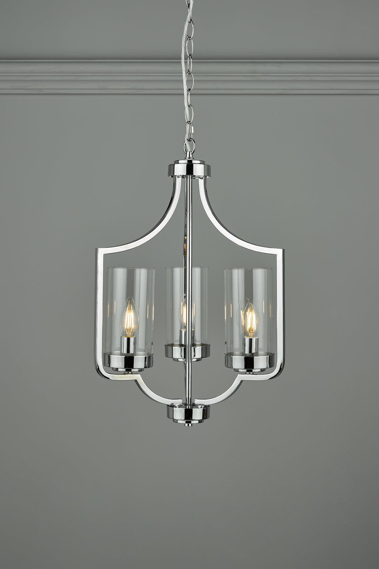 Modern chrome chandelier with three candle-style bulbs and glass shades on grey background