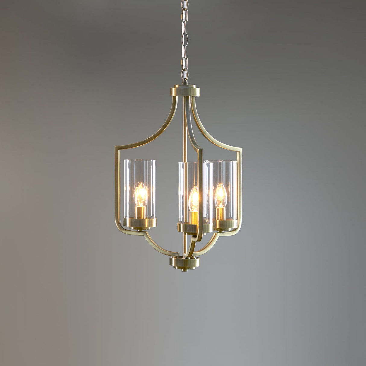 Elegant brass chandelier with three candle-style bulbs and clear glass shades against gray background