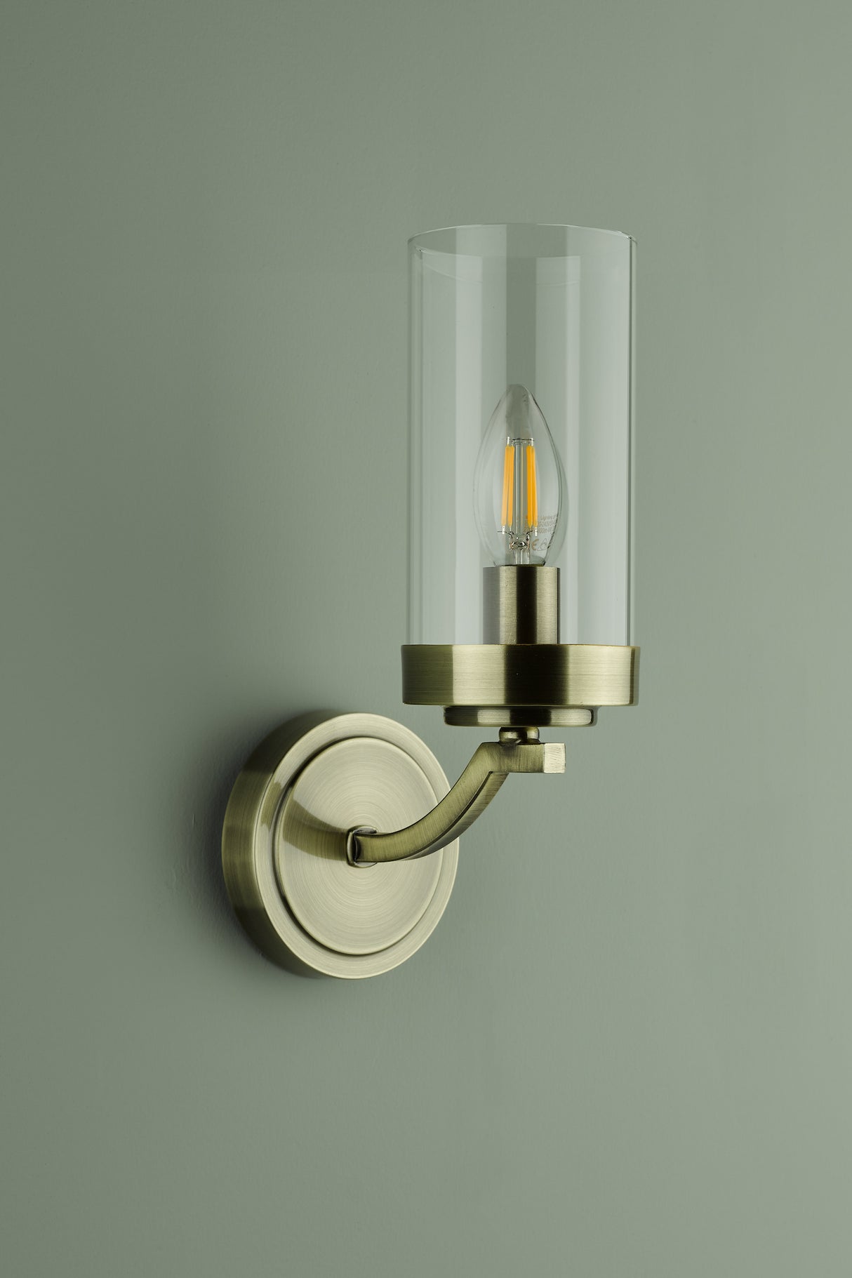 Brass wall sconce with clear glass shade and Edison bulb on pale green wall