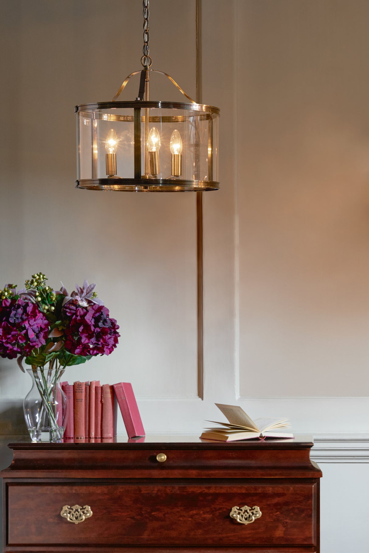 Elegant vintage chandelier above wooden chest with red books, purple flowers, and open book indoors