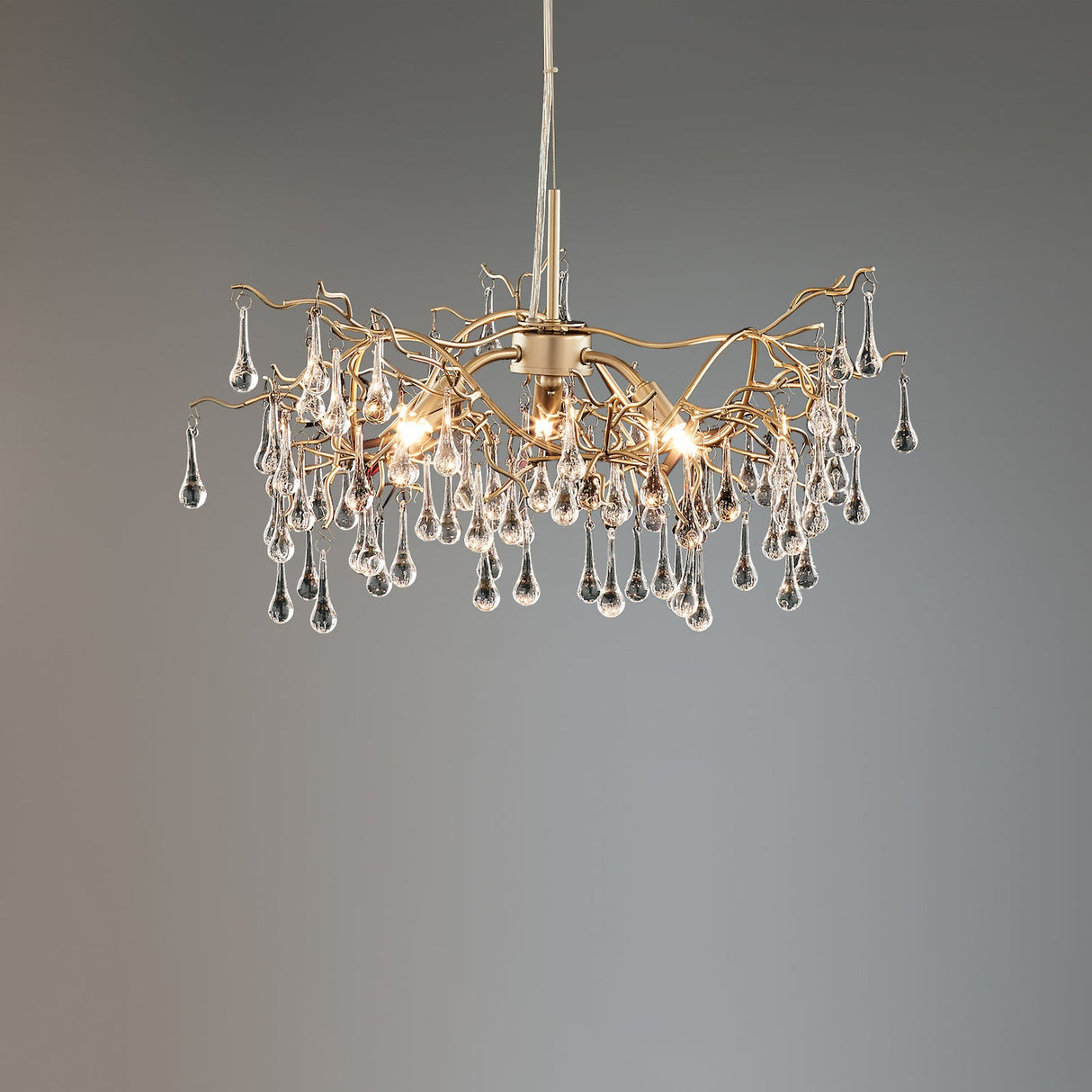 Modern chandelier with gold branches and hanging glass droplet crystals on gray background