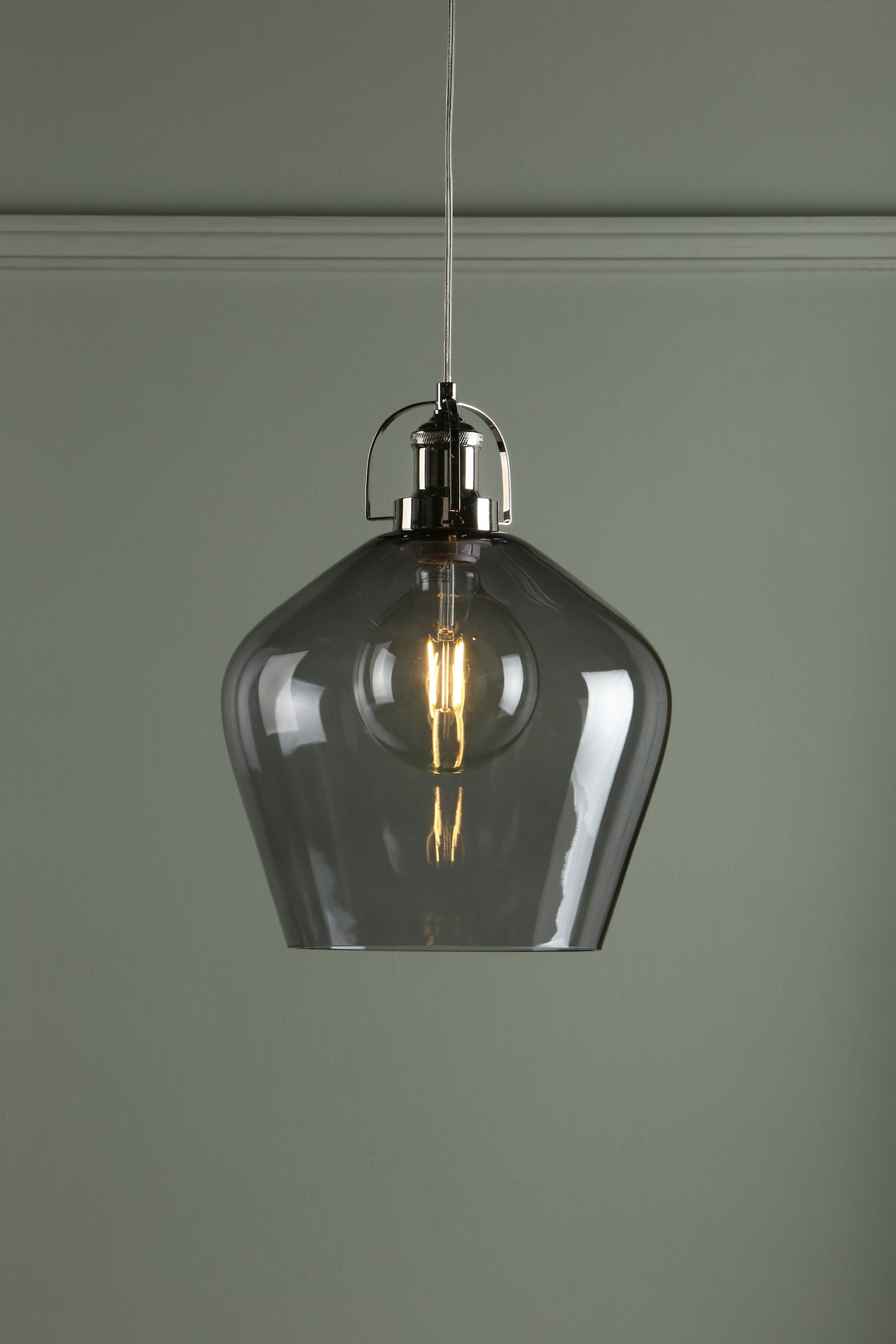 Modern pendant light with transparent smoky glass shade and glowing filament bulb against gray wall