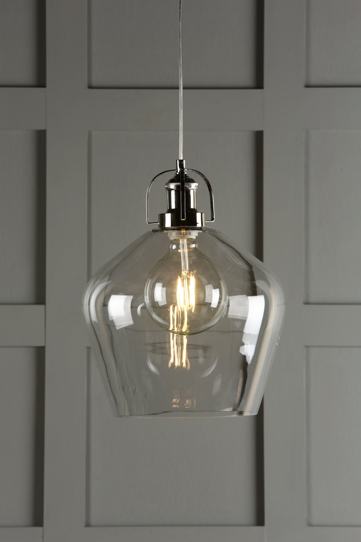Modern pendant light with clear glass shade and exposed filament bulb against gray paneled wall
