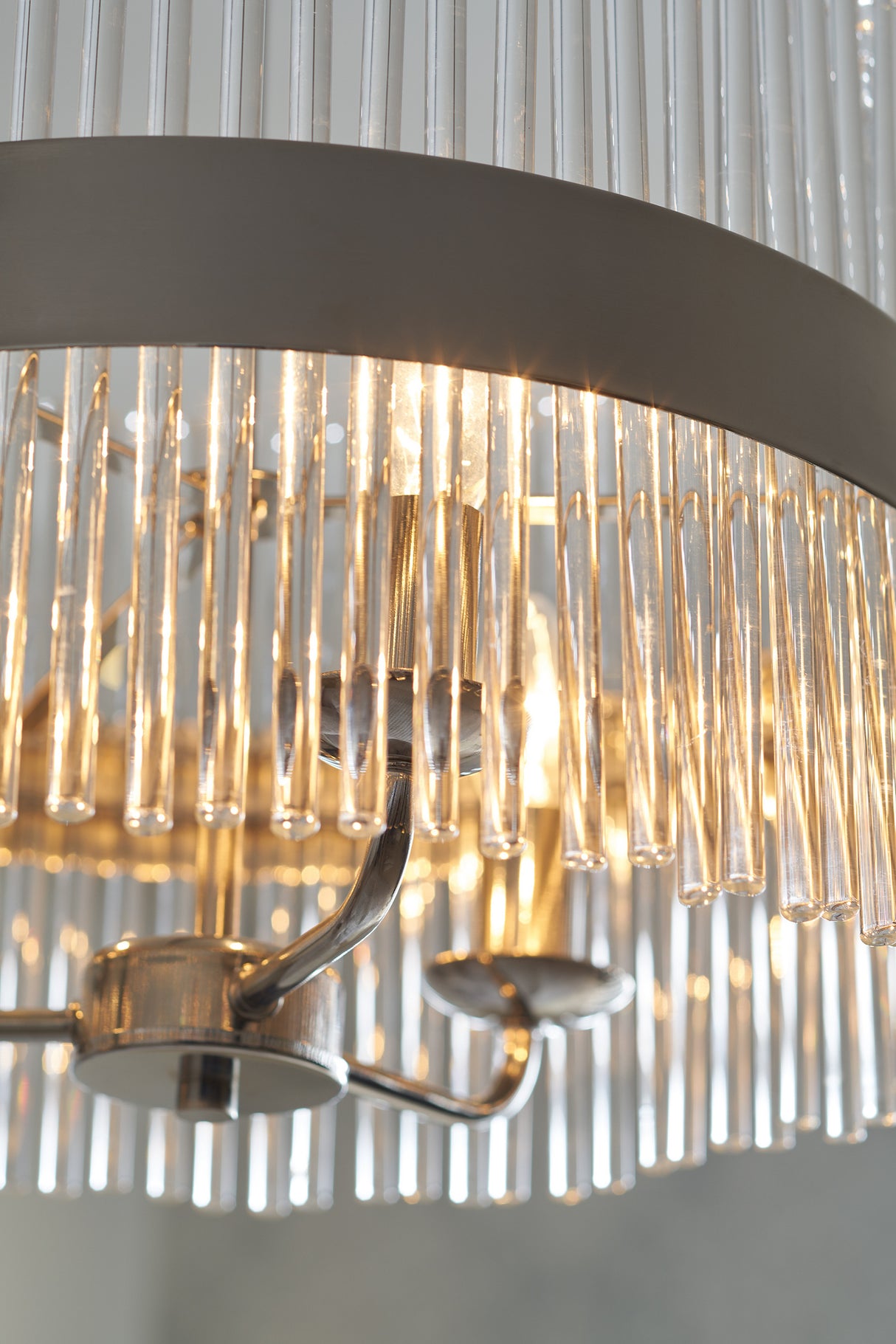 Close-up of modern chandelier with clear glass rods and polished metal arms glowing warmly