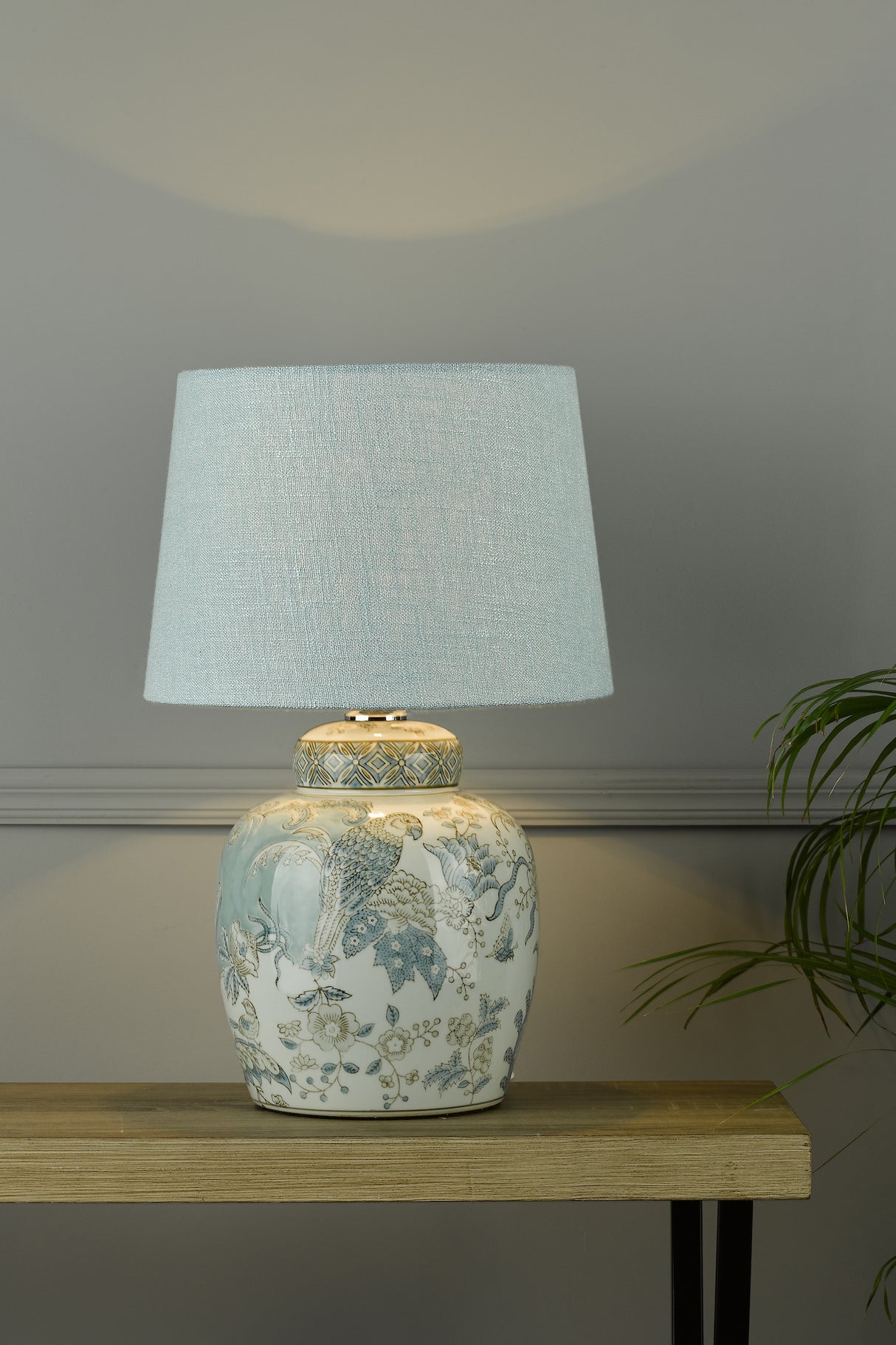 Ceramic table lamp with blue floral and bird design and light blue fabric shade on wooden table