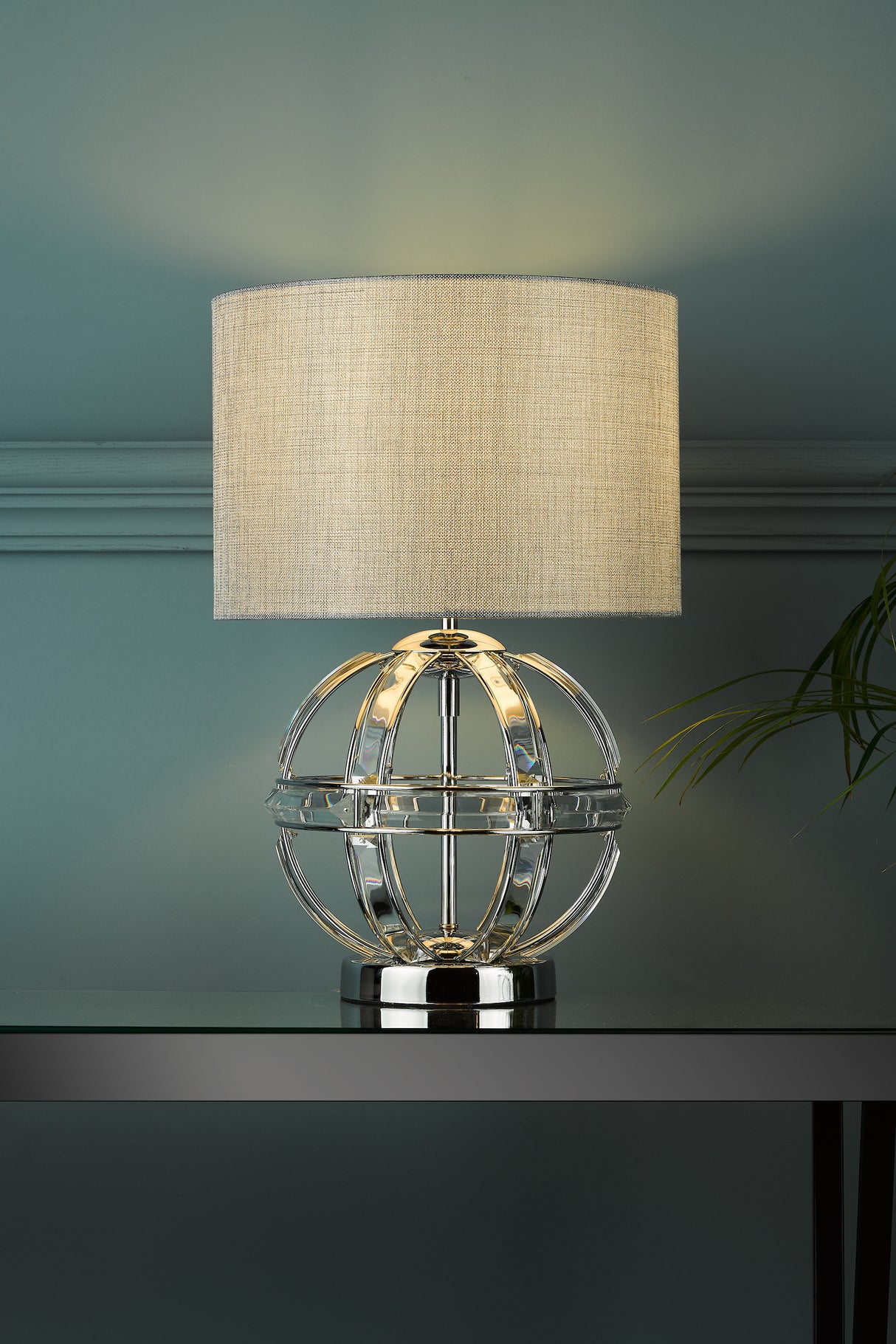 Modern table lamp with beige fabric shade and chrome circular base on glass top table