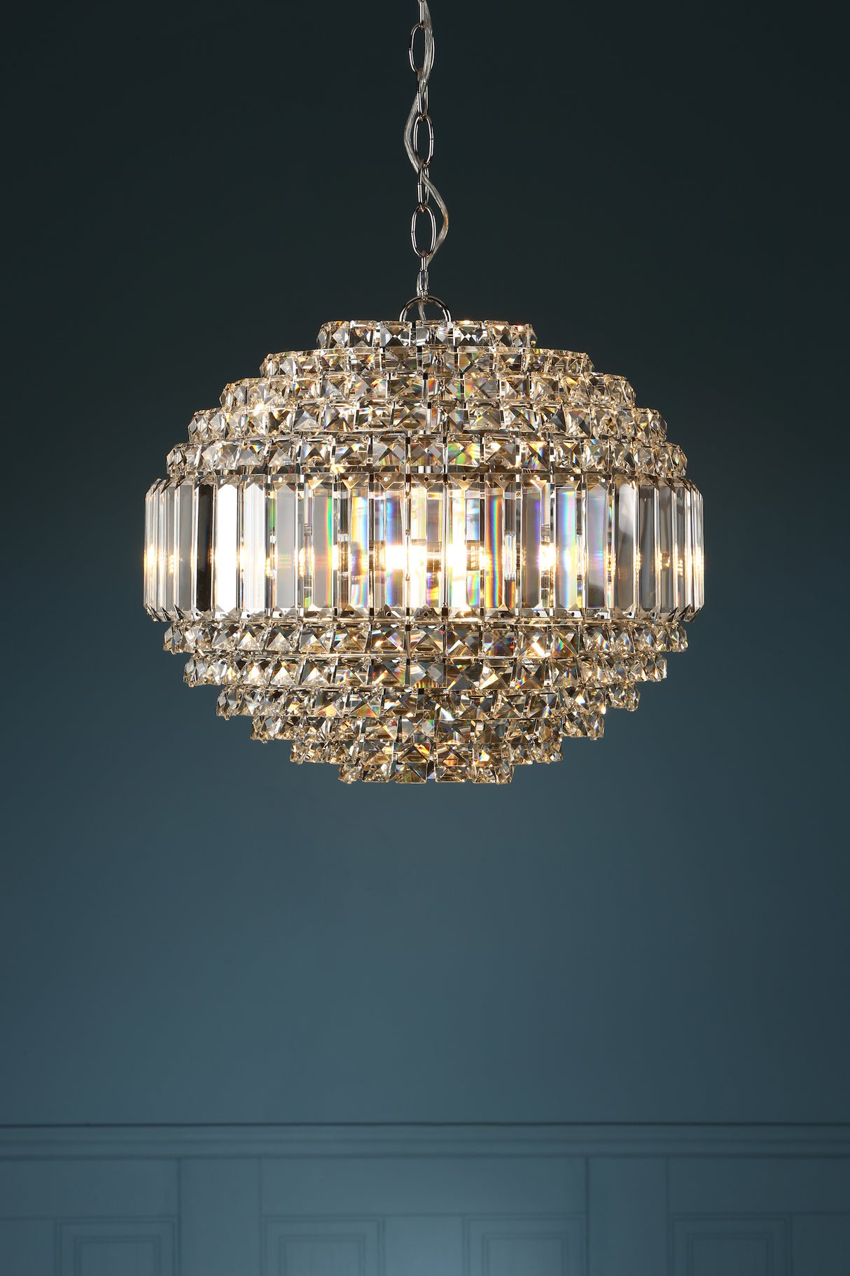 Elegant crystal chandelier pendant light with silver chain against dark blue wall