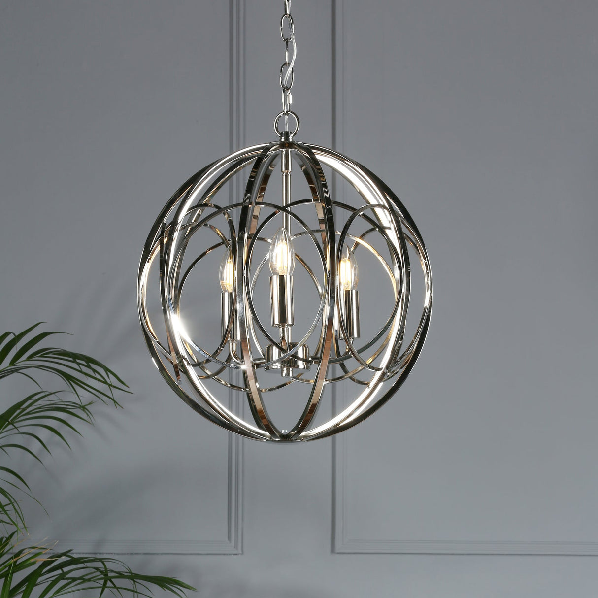 Modern chrome orb chandelier with three candle-style bulbs hanging in a gray room with plant