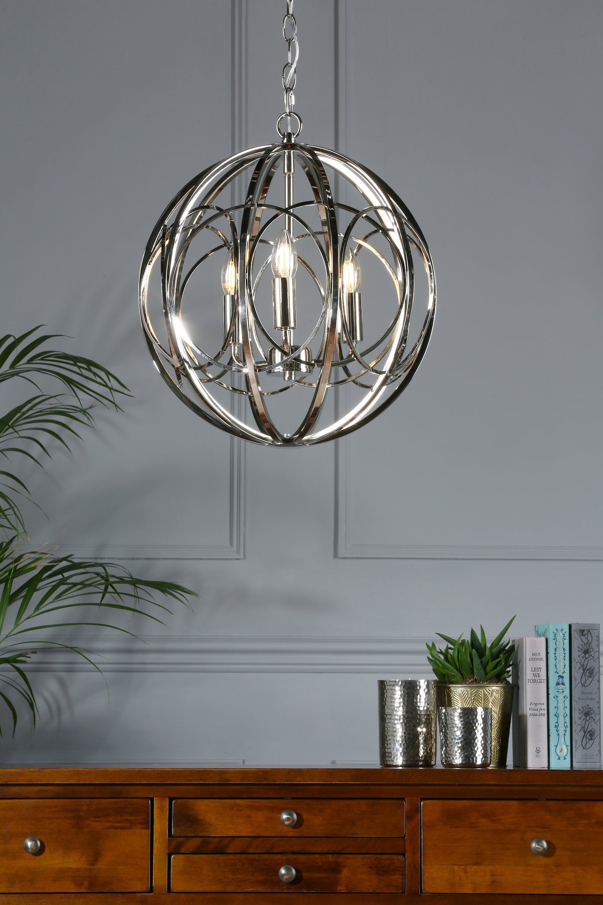 Modern chrome orb chandelier with candle lights over wooden dresser with plants and books