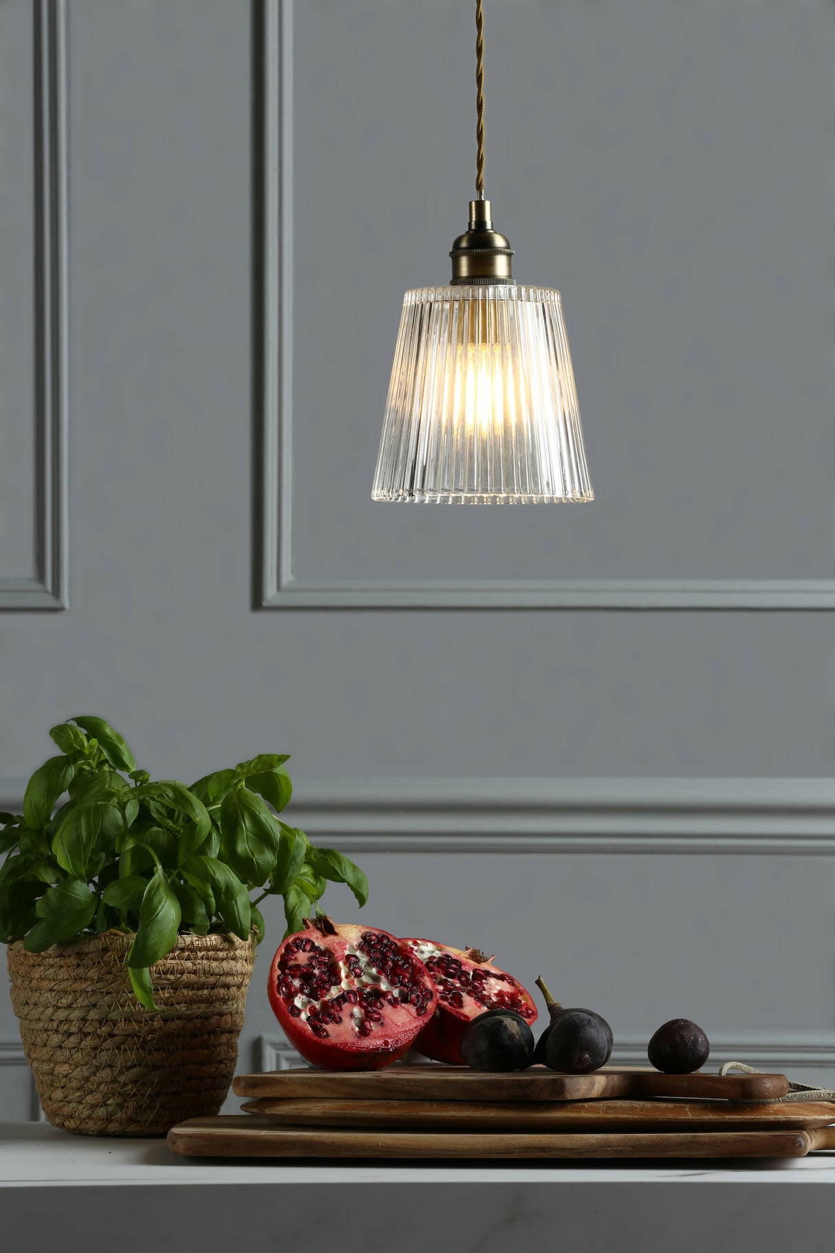 Modern pendant light above countertop with potted basil, sliced pomegranate, and grapes on wooden boards