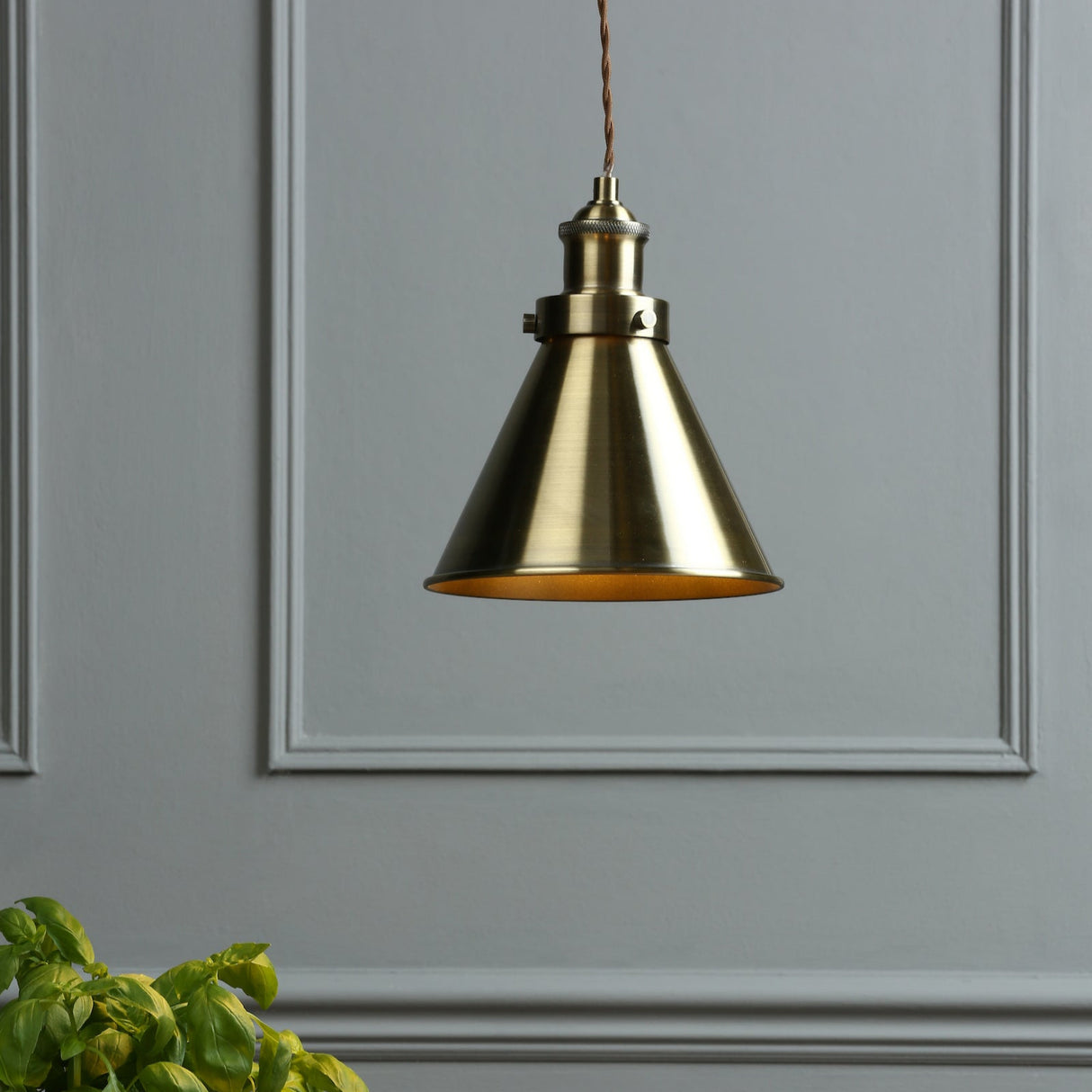 Brushed brass pendant light with conical shade hanging against gray wall with molding