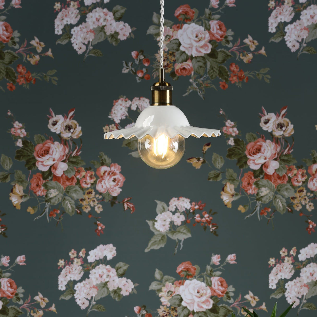 White pendant light with ruffled ceramic shade and filament bulb against floral wallpaper
