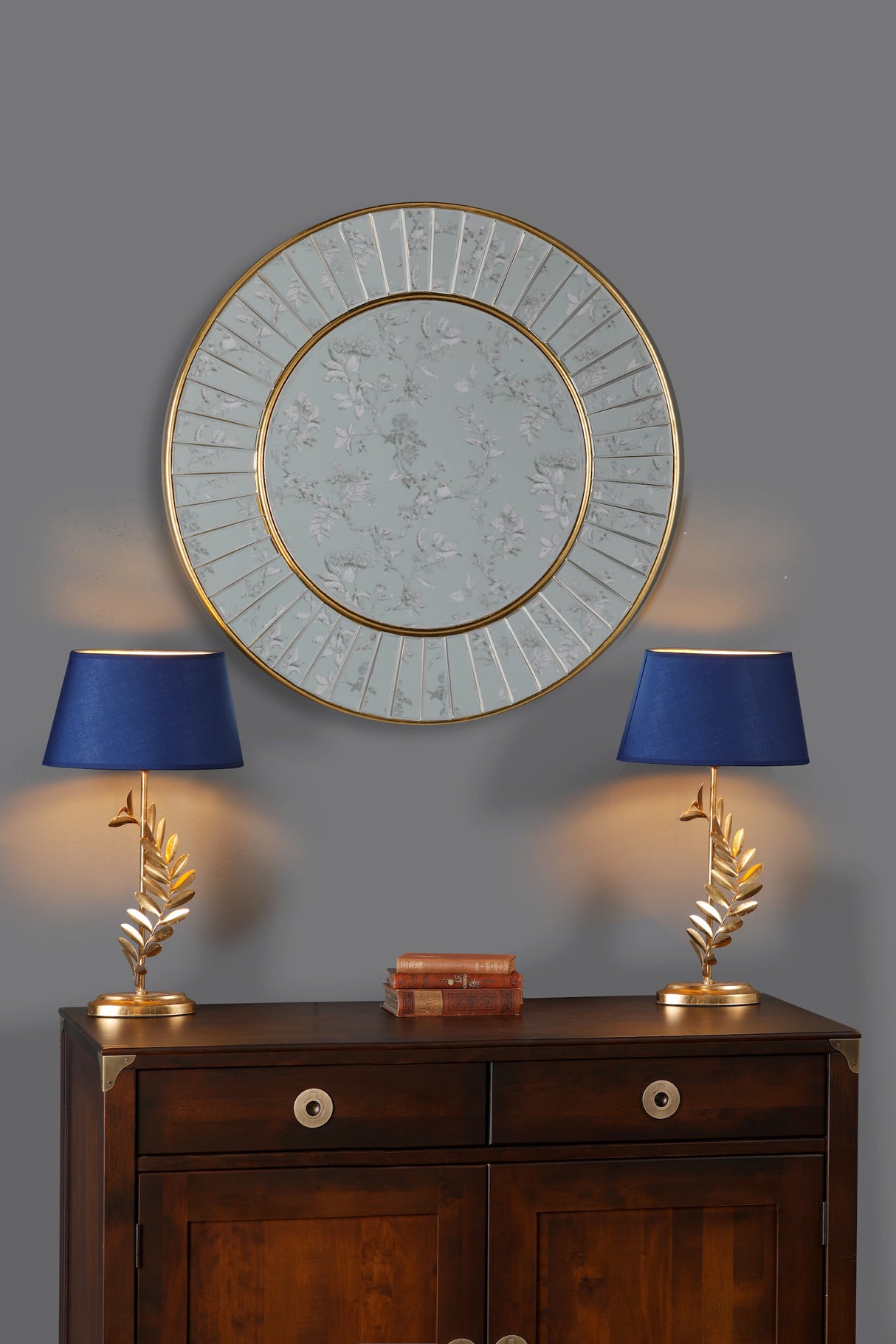 Dark wood cabinet with two gold and blue lamps and round decorative mirror on gray wall