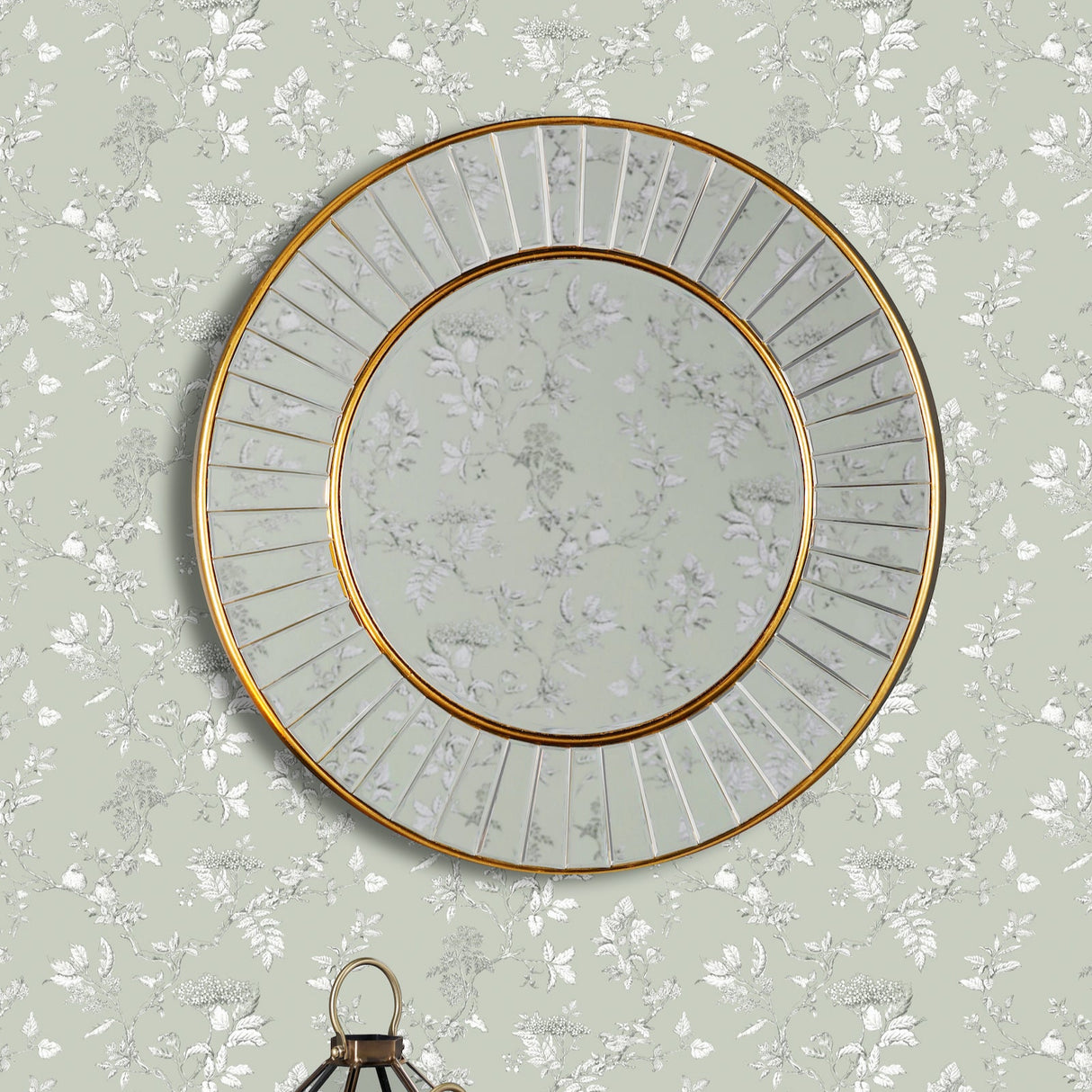 Round gold-framed mirror on pale green floral wallpaper with decorative lantern below
