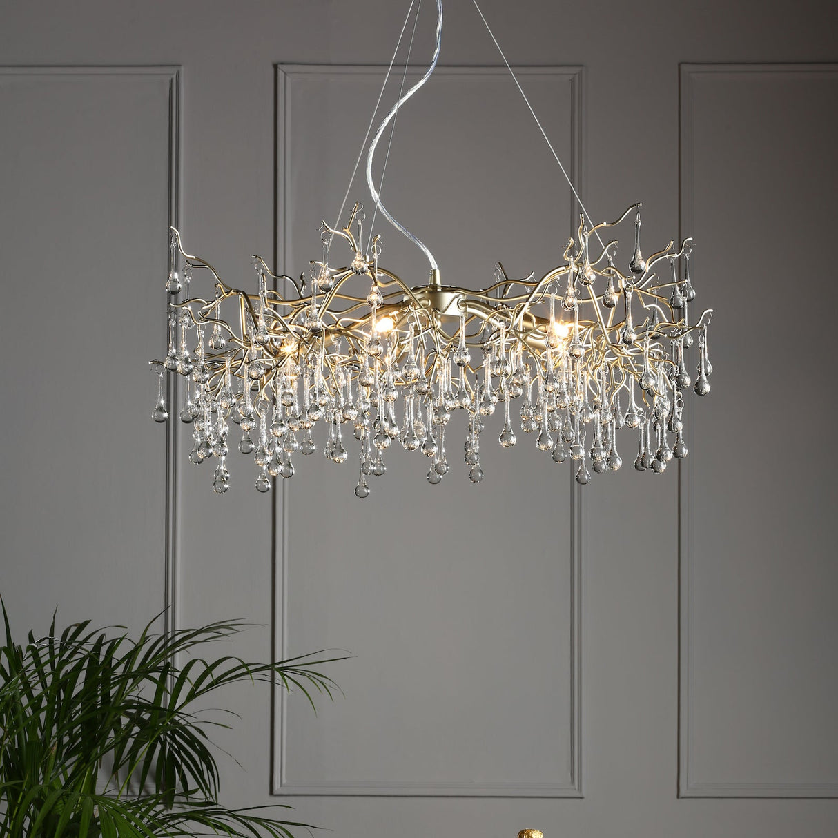 Modern chandelier with gold branches and clear glass droplets hanging in a gray room